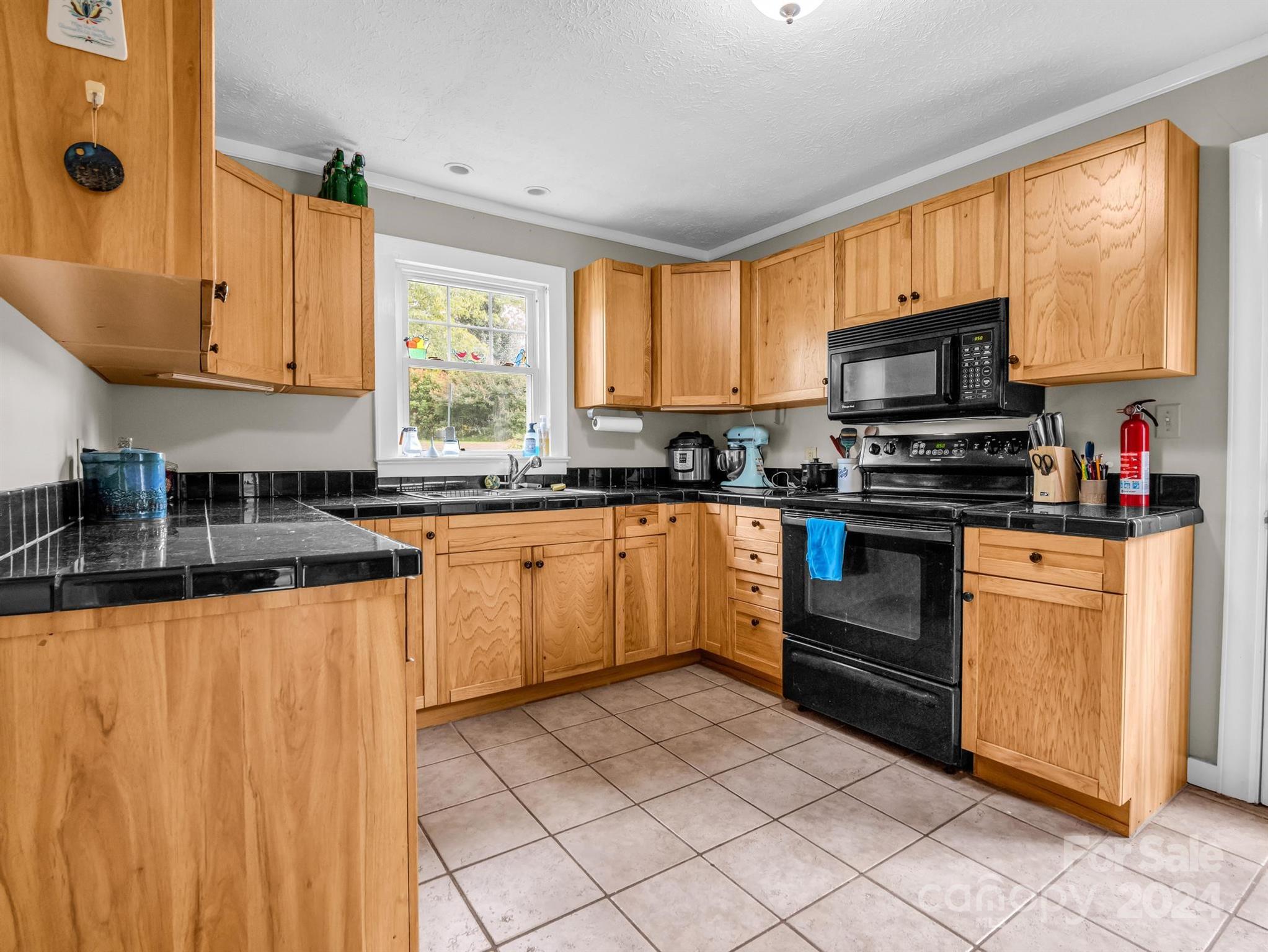 Kitchen with honey-colored wood cabinets, black tile counters, and a window above the sink.