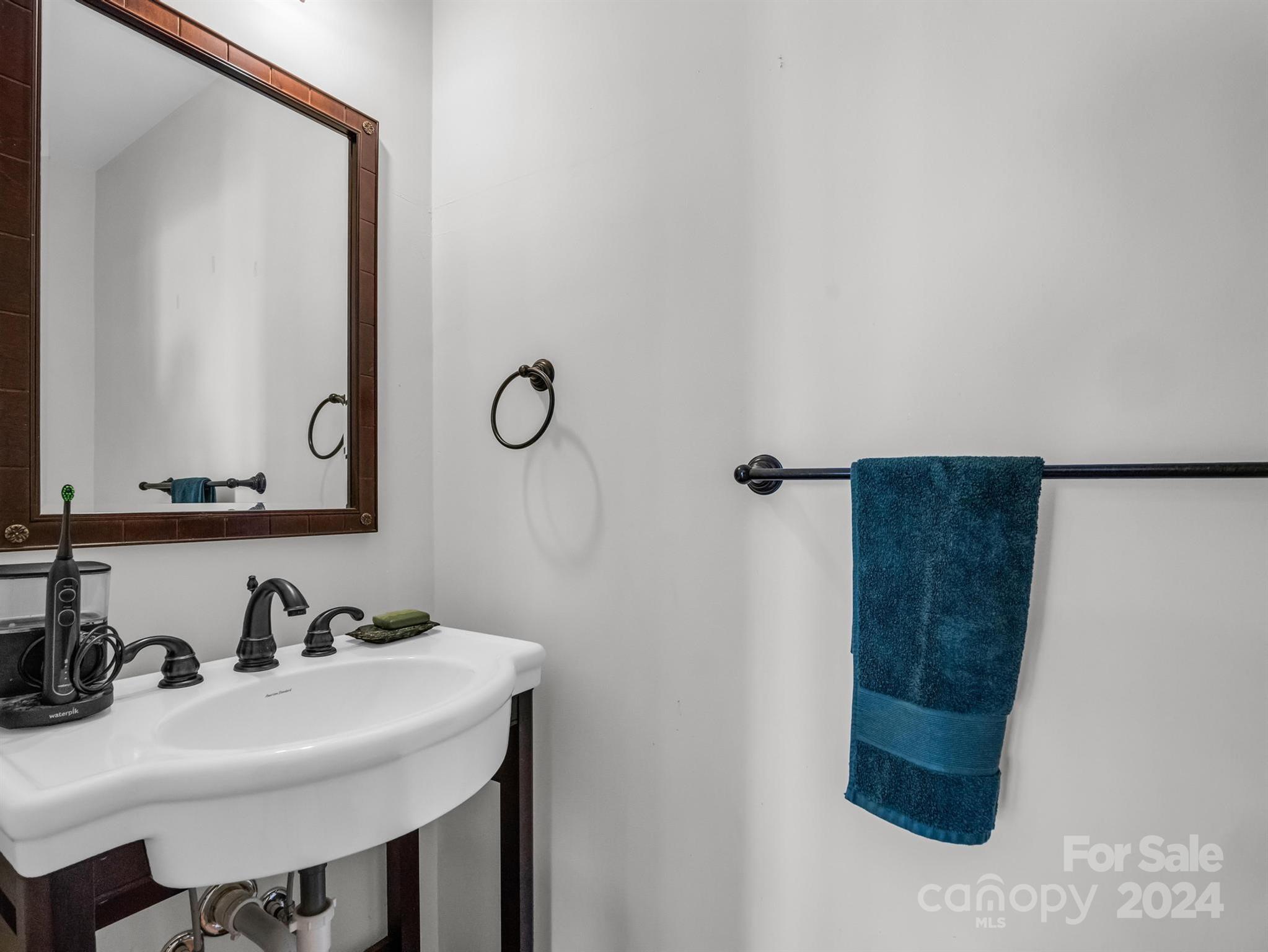Bathroom vanity with a white sink, dark bronze fixtures, wood-framed mirror, and blue towel.