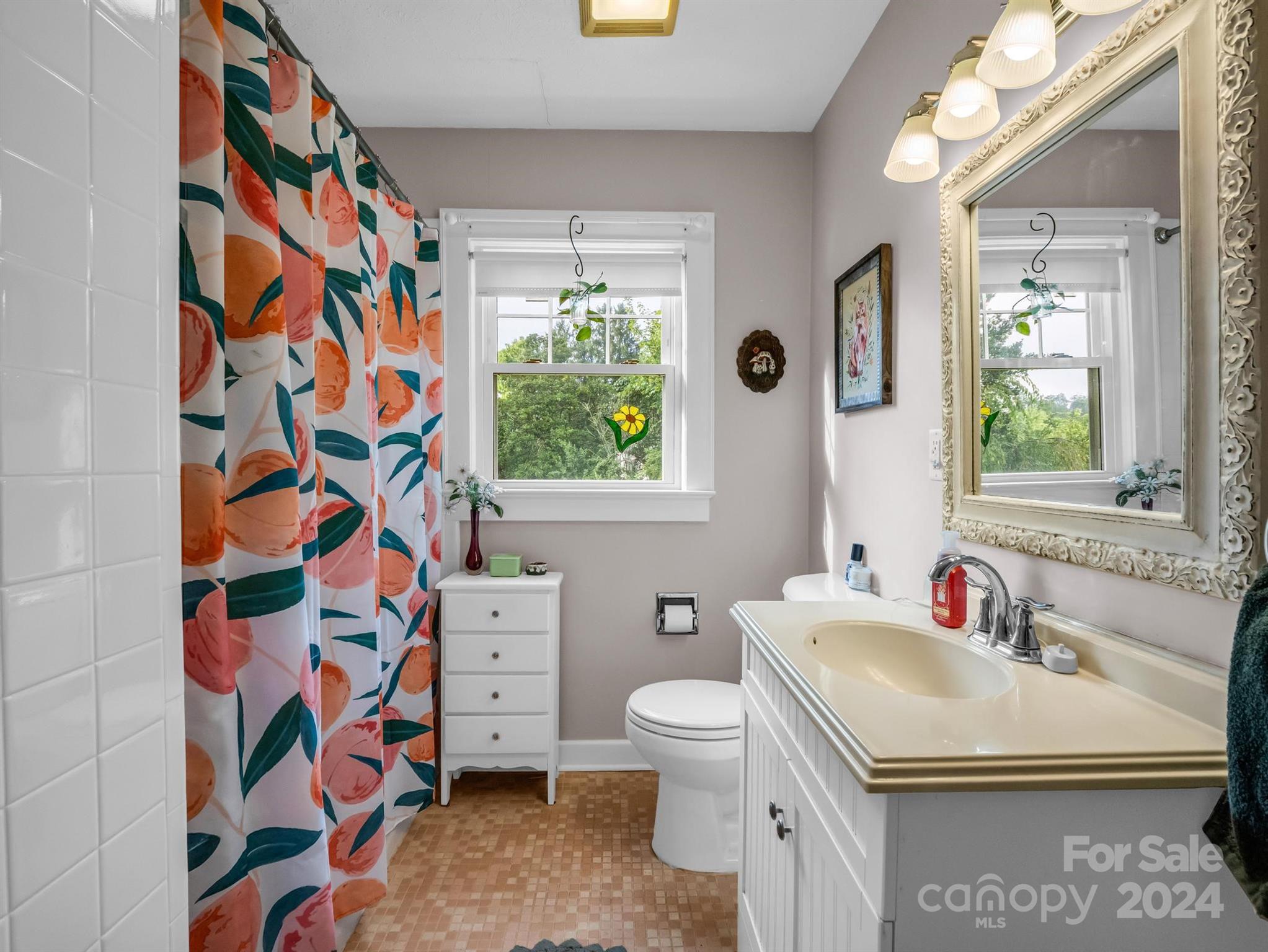 Bathroom with a cream sink, ornate mirror, and orange-and-teal floral shower curtain.