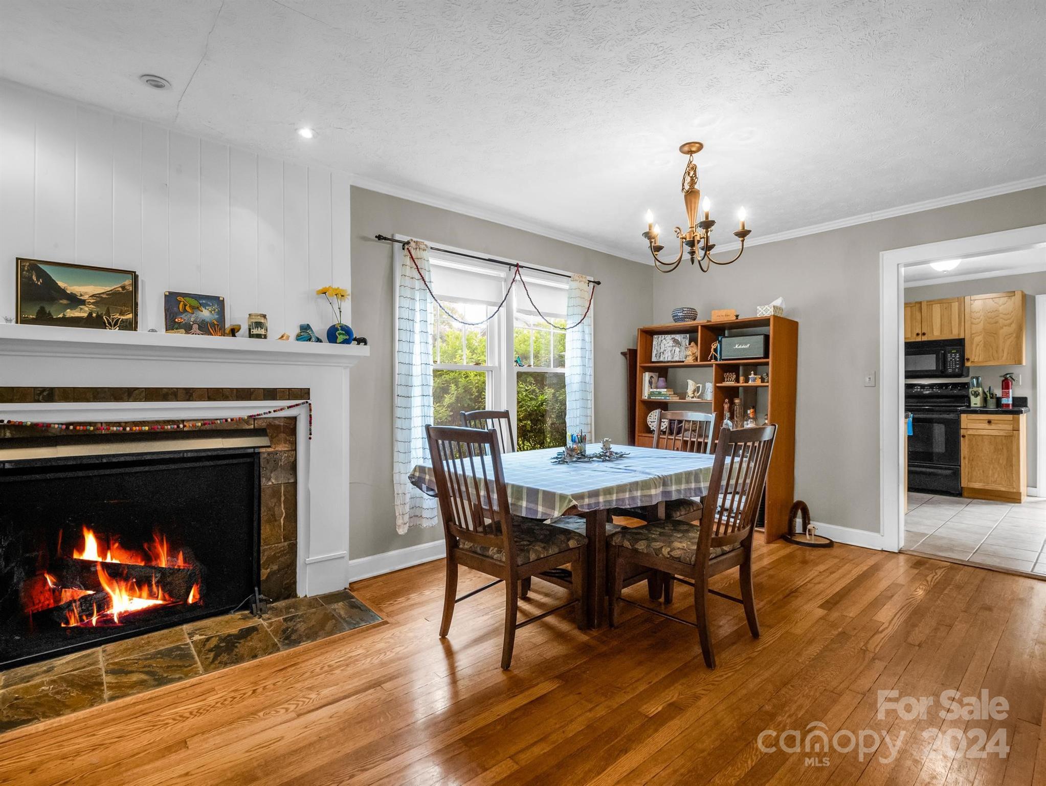 Dining room with a lit fireplace, hardwood floors, and a table beside a bright window.