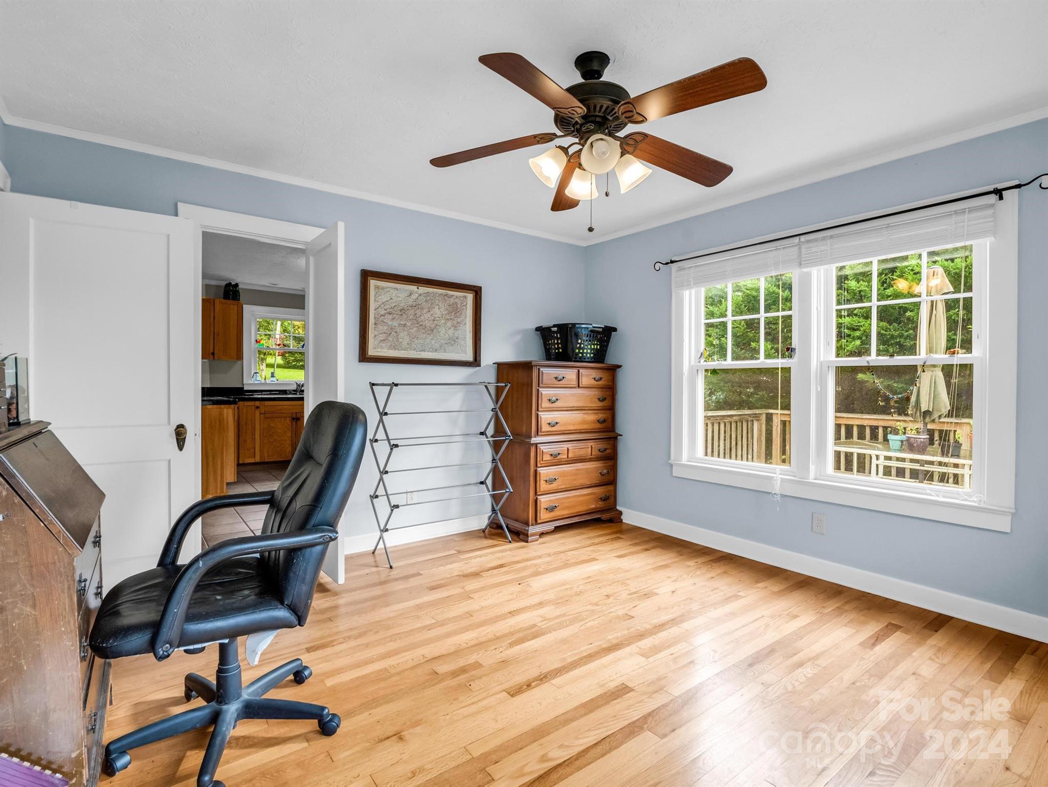 Home office with hardwood floors, a black chair, wooden dresser, and windows overlooking a deck.