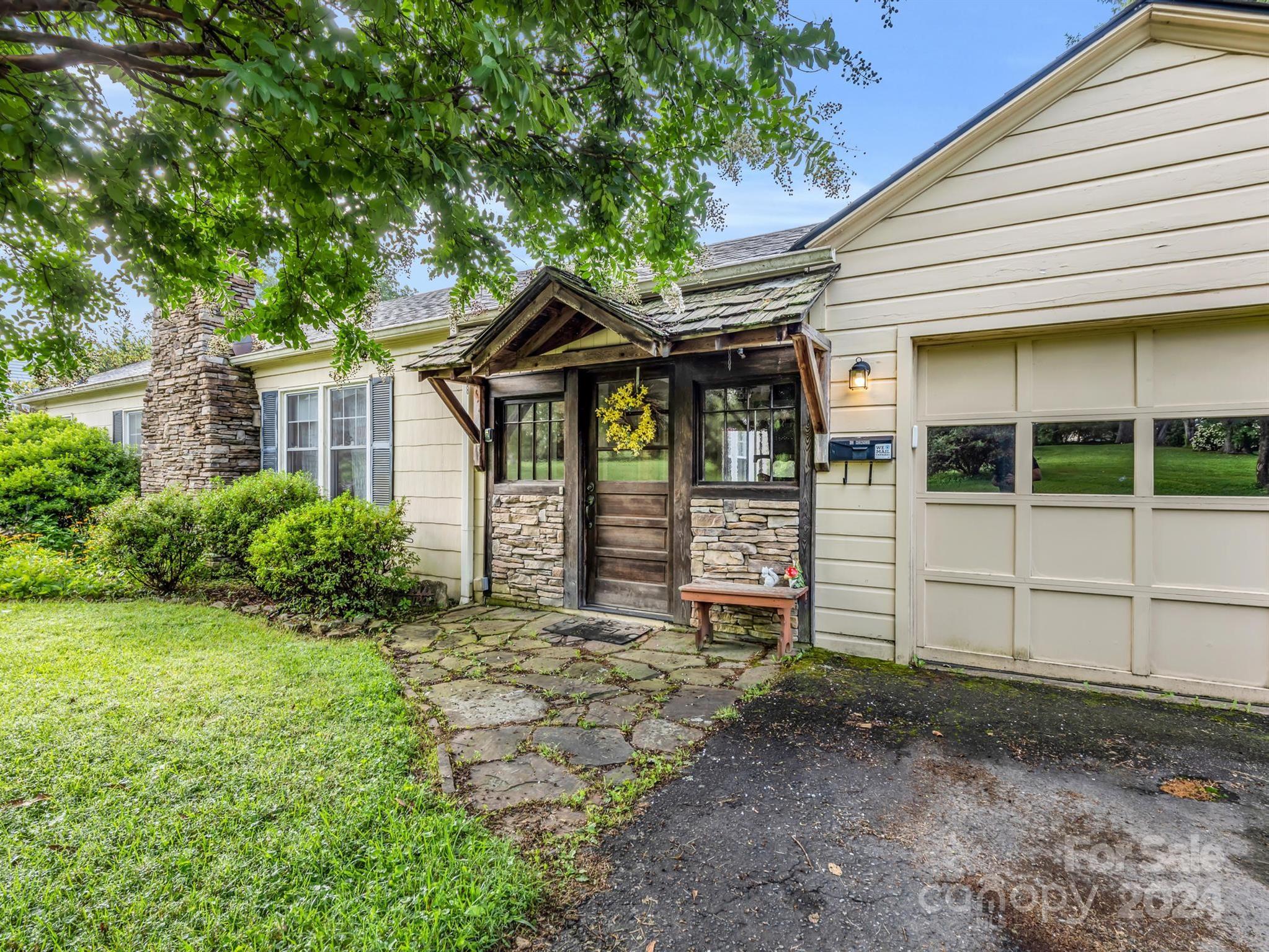Home exterior with a rustic timber-and-stone entry, stone chimney, and attached garage.