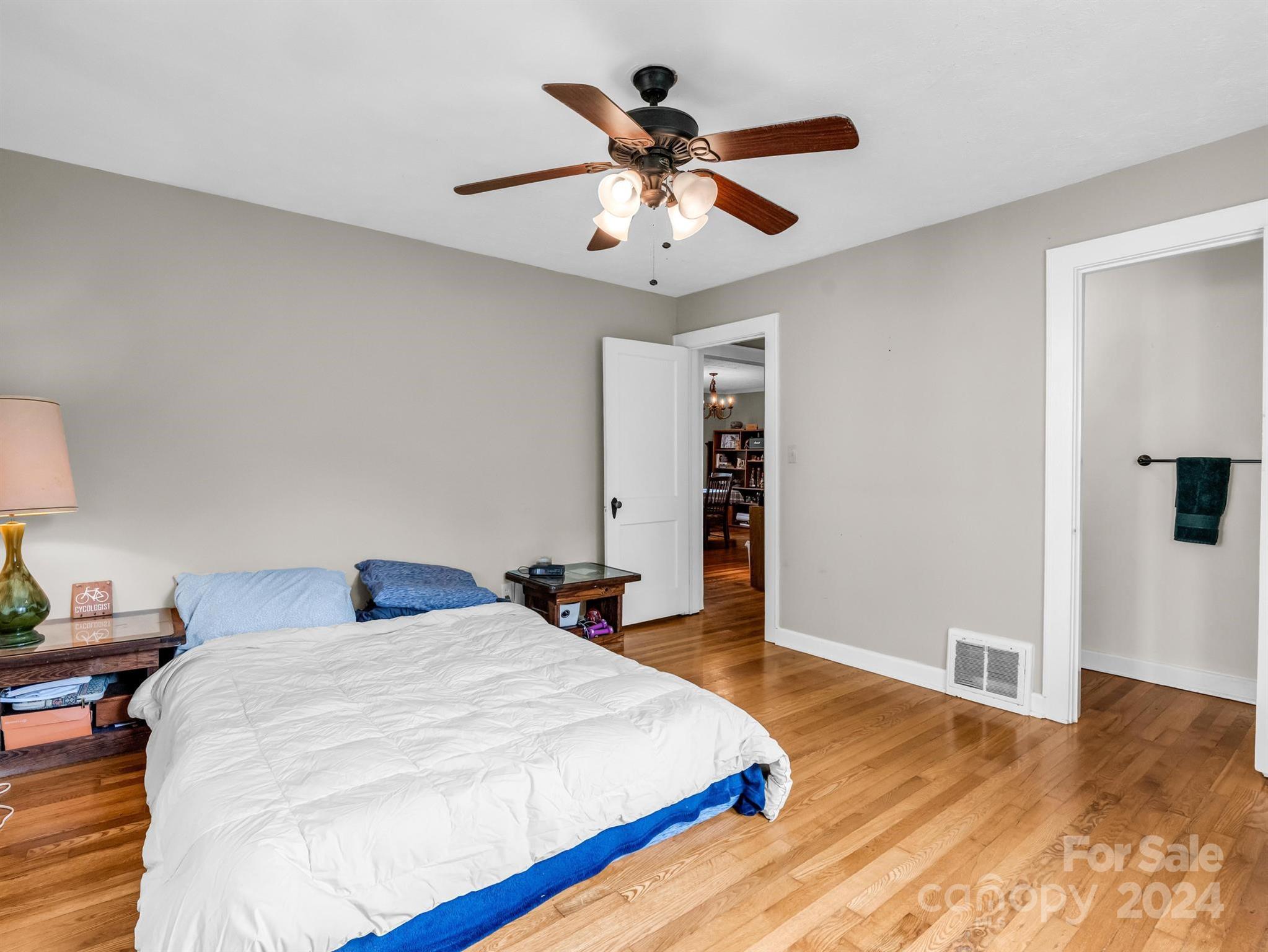 Bedroom with a white duvet, blue bedding, hardwood floors, and a ceiling fan.