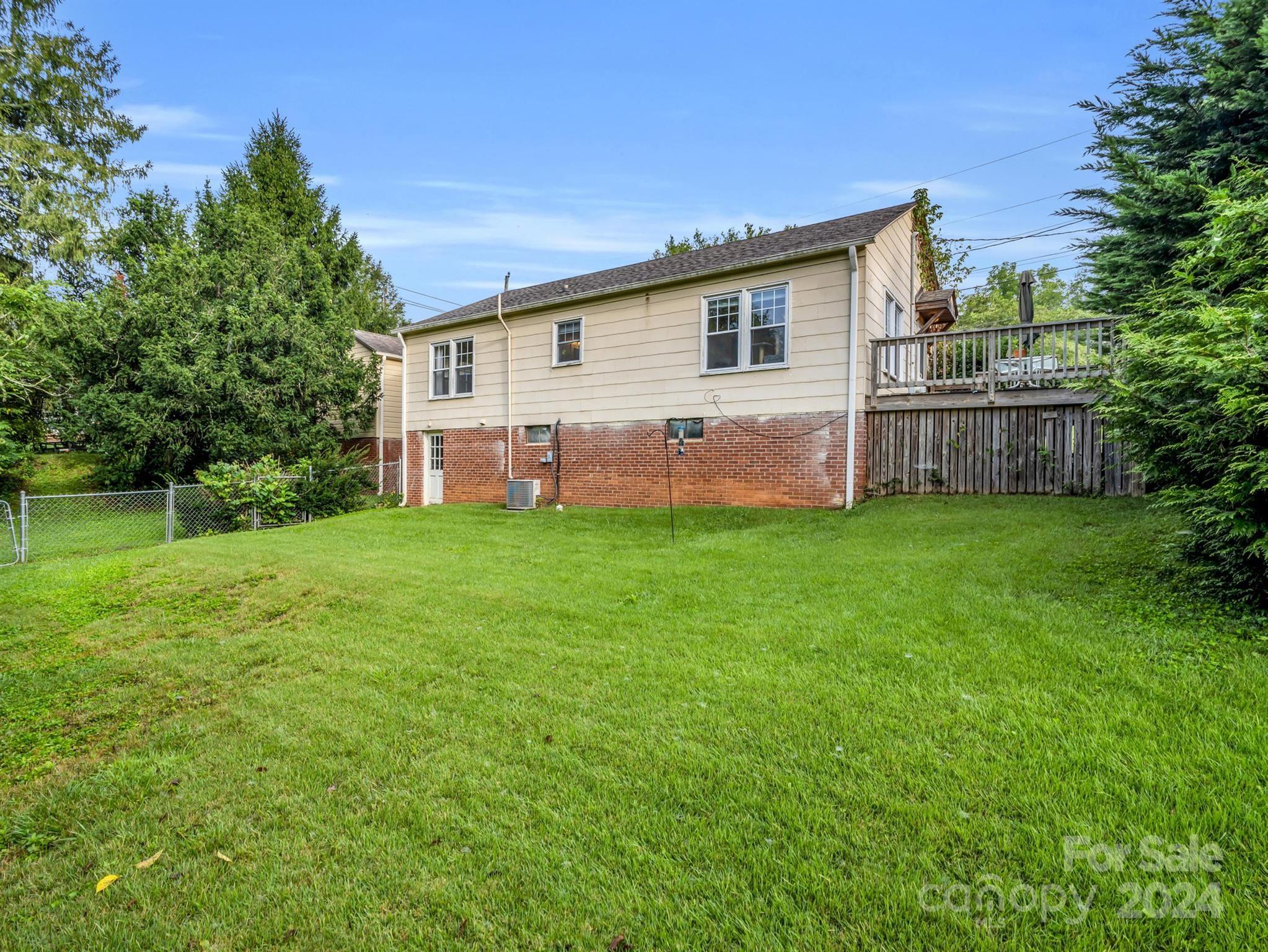 Rear of a two-story house with a raised deck, brick lower level, and broad grassy lawn.