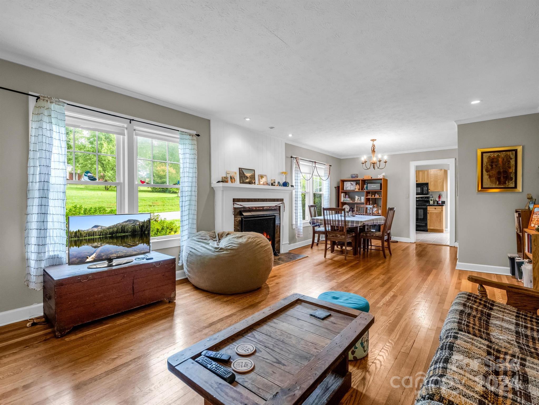 Living and dining room with hardwood floors, a fireplace, large windows, and a dining table.
