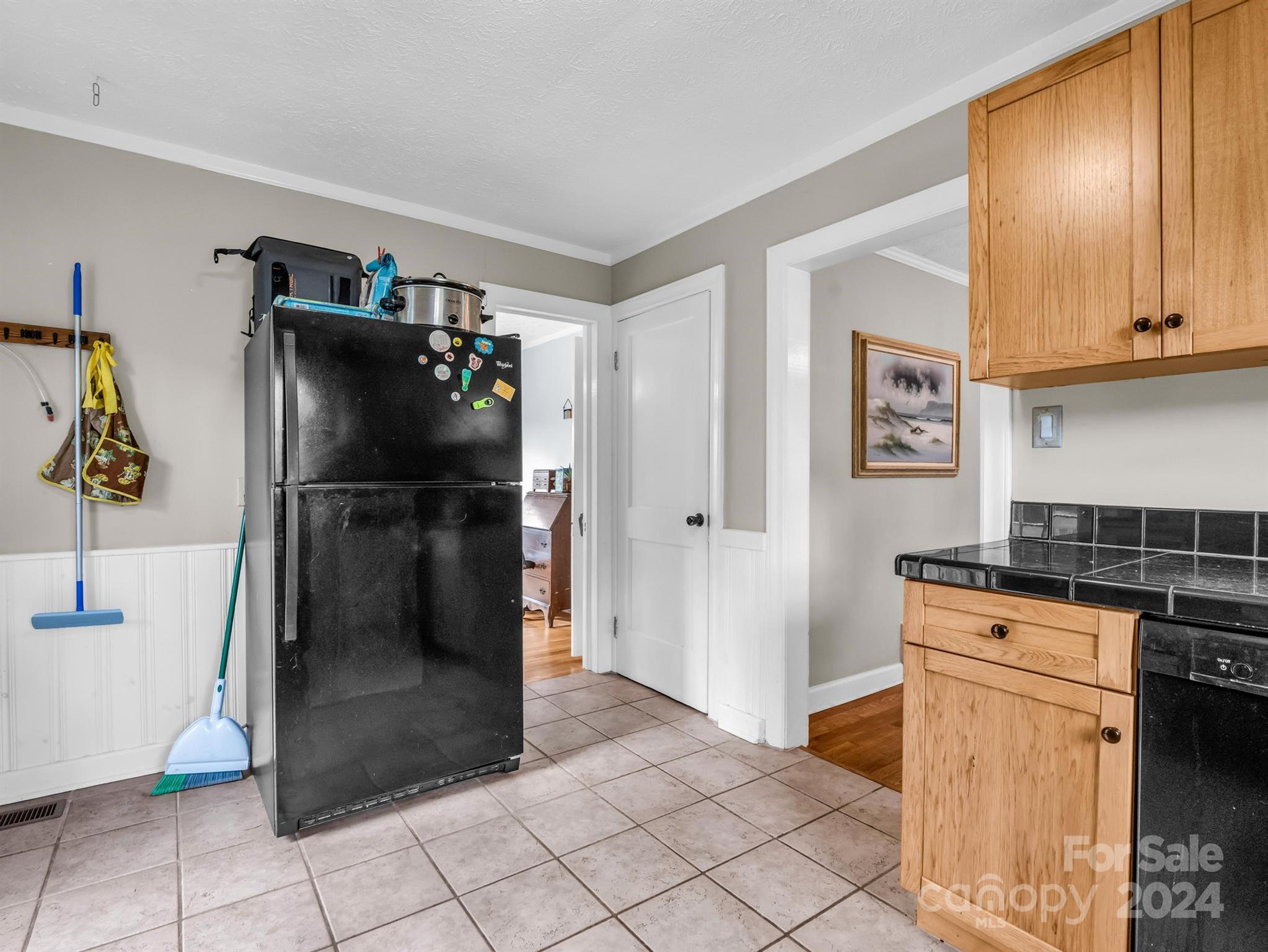 Kitchen with a black refrigerator, light wood cabinets, and black tile countertops.