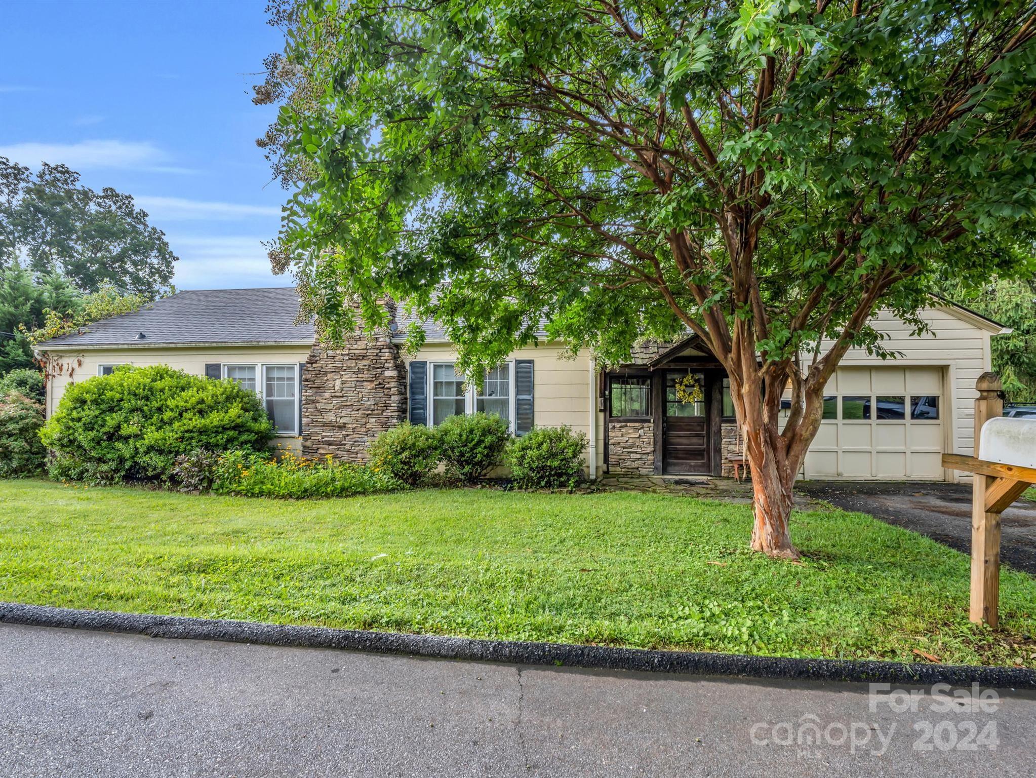 Single-story home with stone chimneys, an attached garage, and a large shade tree over the lawn.