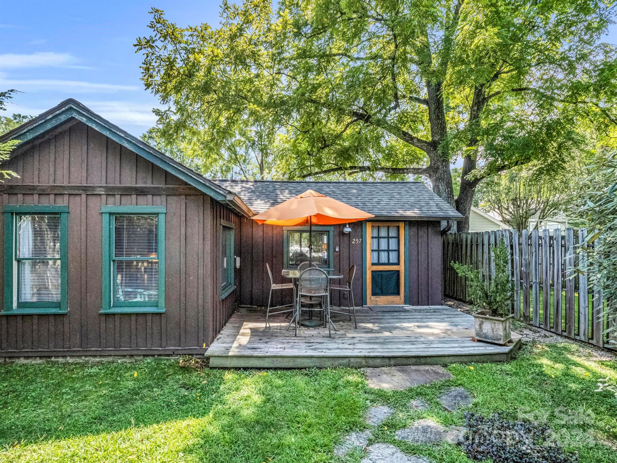 Brown home with teal trim and a deck furnished with patio chairs beneath an orange umbrella.