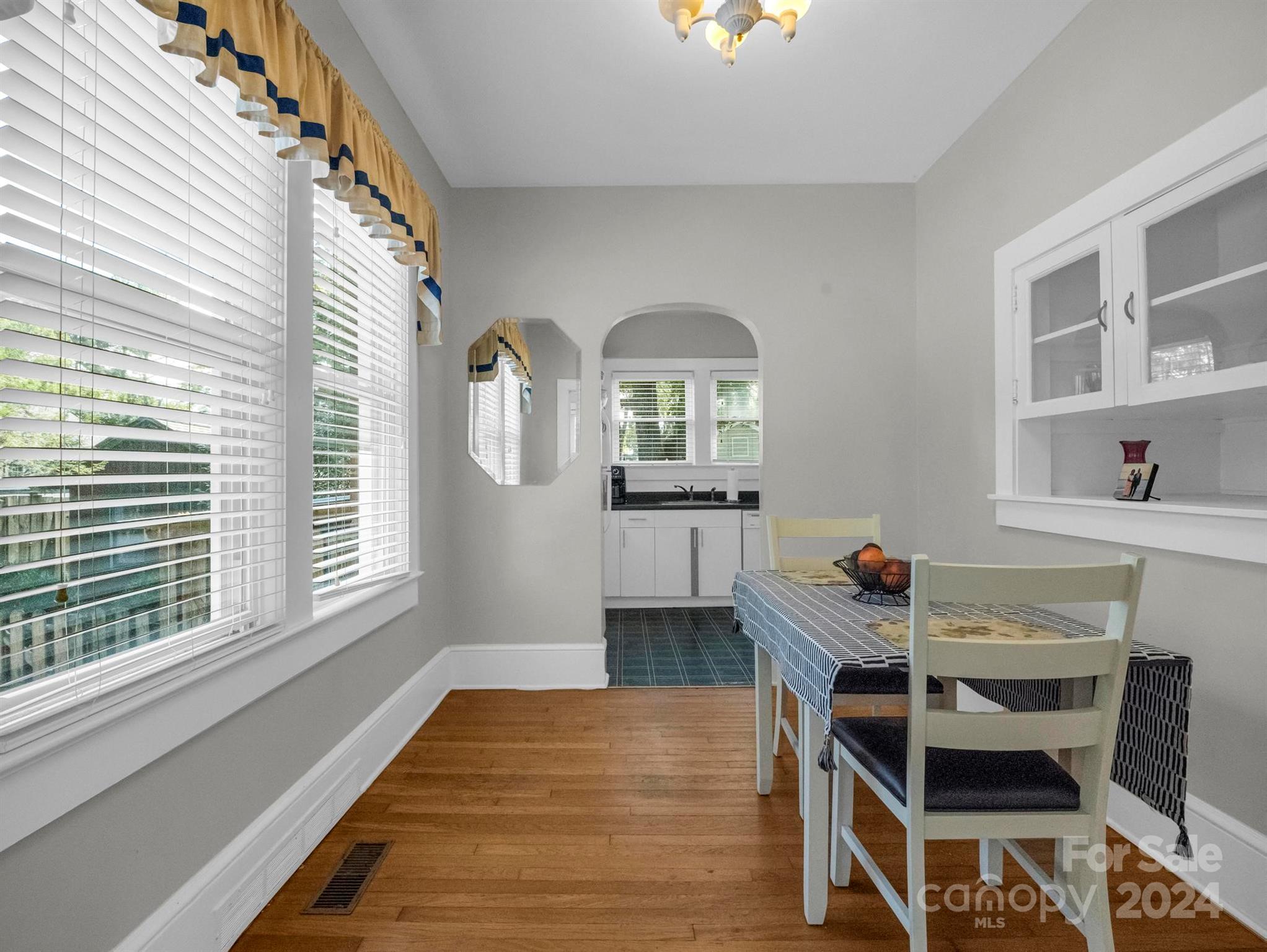 Dining area with hardwood floors, large shuttered windows, and an arched opening to the kitchen.
