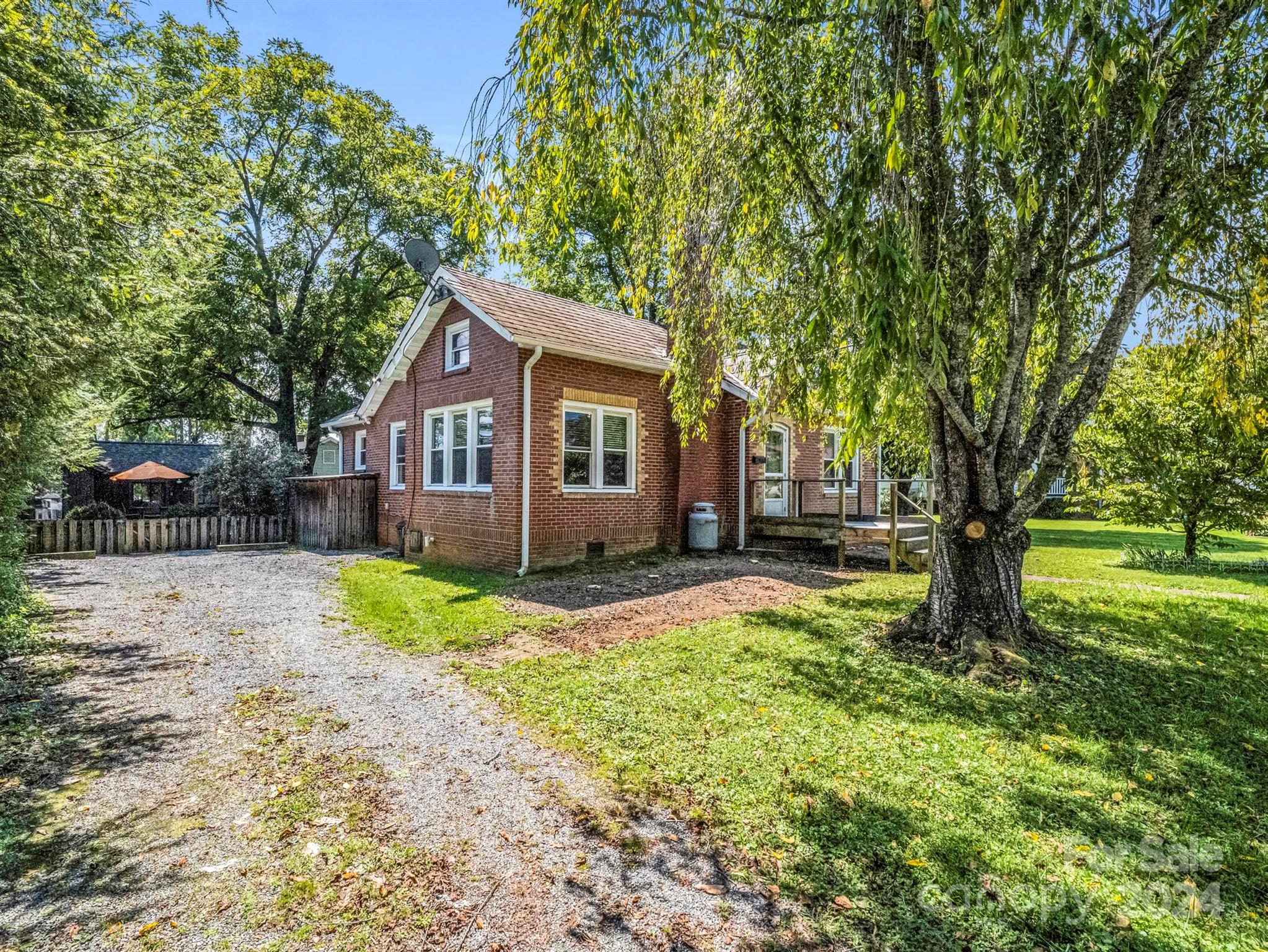 Red brick house with a raised deck, gravel driveway, and mature trees shading the yard.