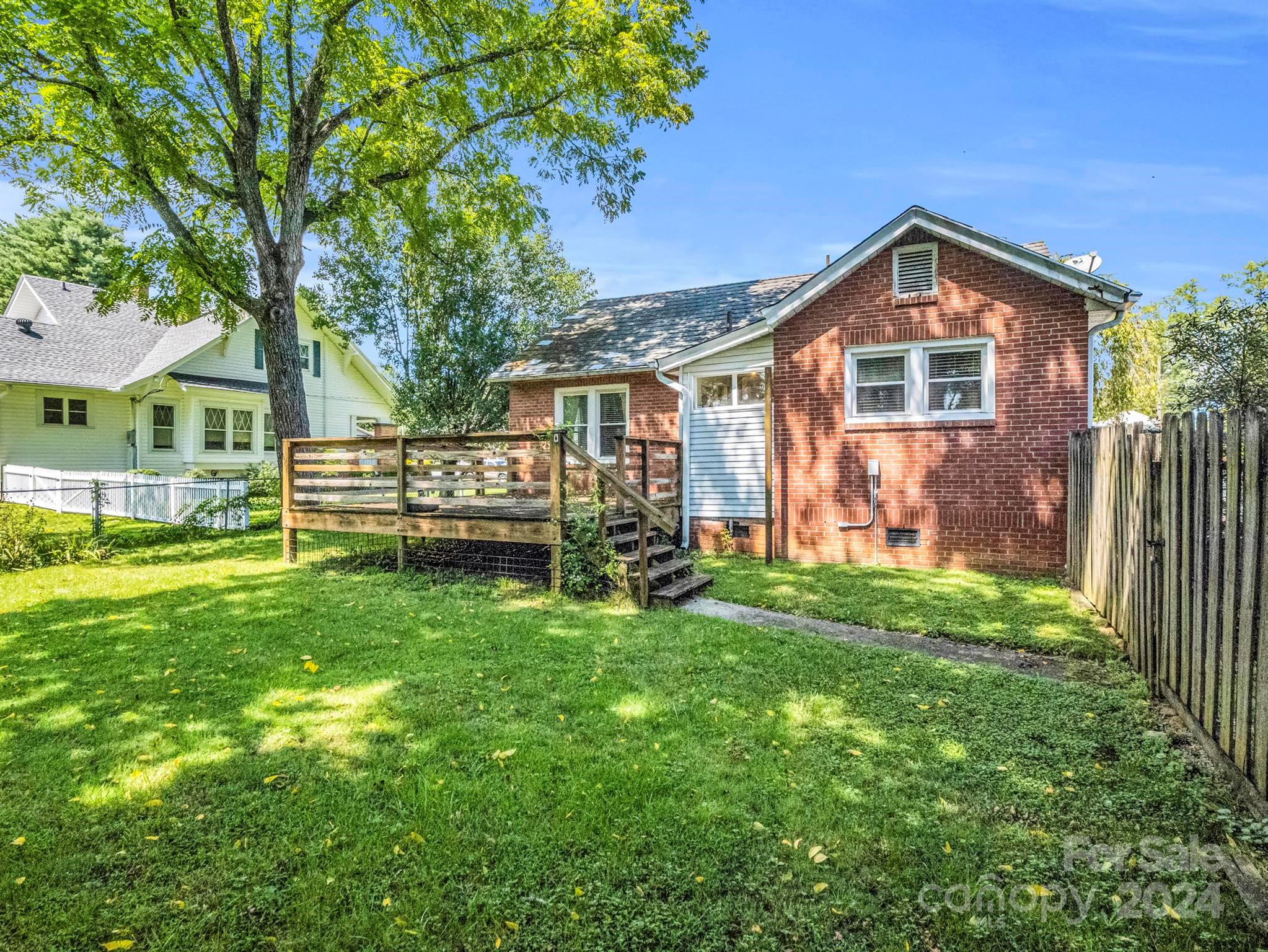 Red brick house with a raised wooden deck overlooking a grassy backyard and privacy fence.