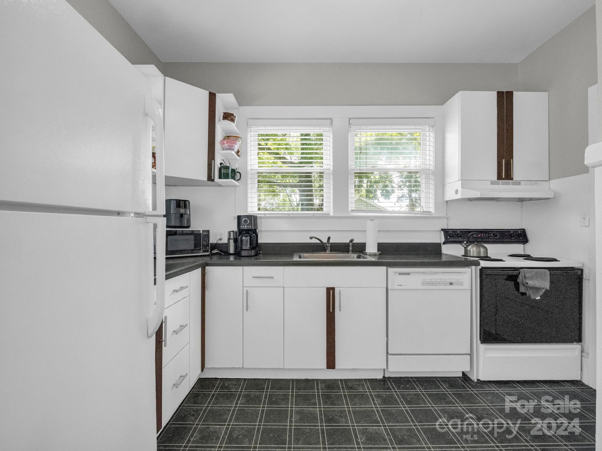 Kitchen with white cabinets, dark countertops, tiled floor, and two windows above the sink.