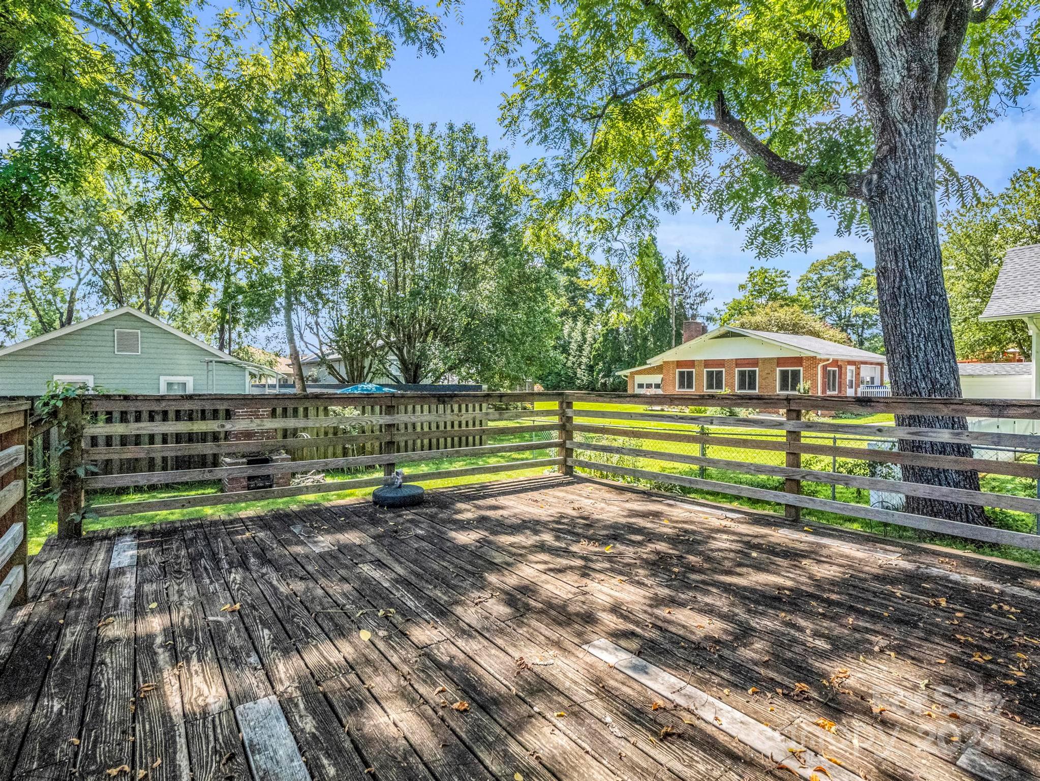 Weathered wooden deck beneath a large tree, overlooking a grassy yard and nearby homes.