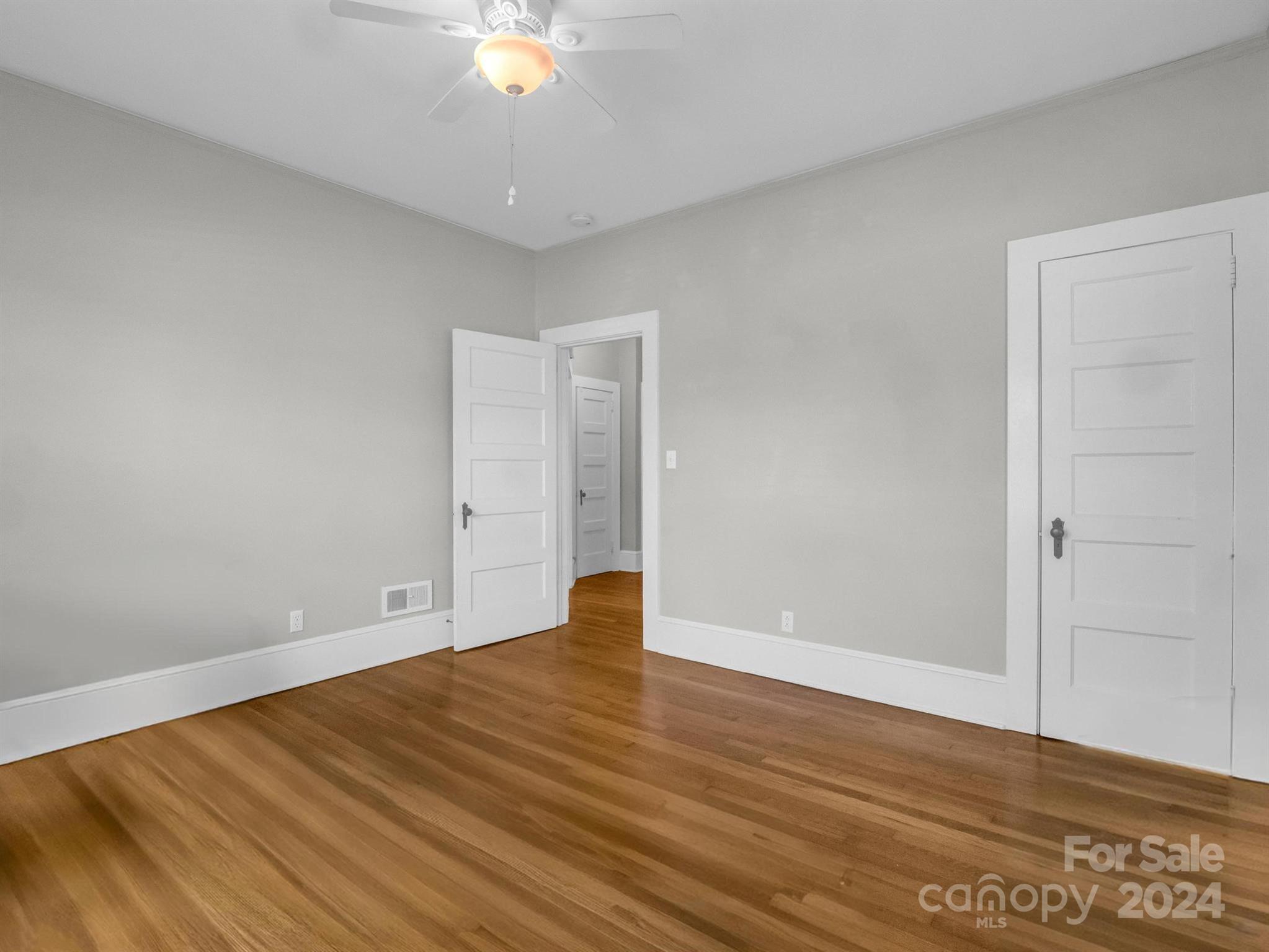 Empty room with hardwood floors, gray walls, white paneled doors, and a ceiling fan.