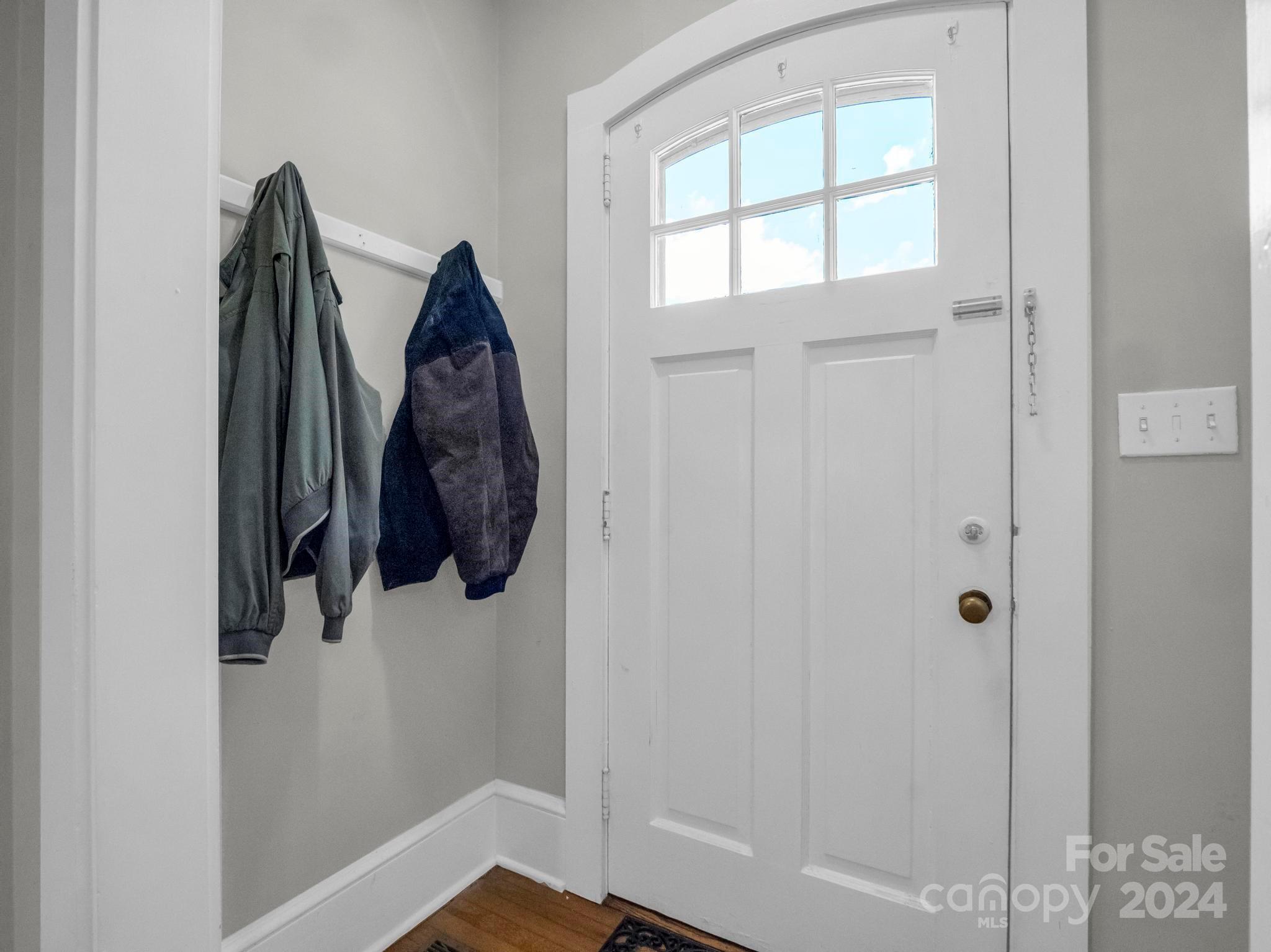 Entryway with a white front door, upper glass panes, and two jackets hanging on wall hooks.