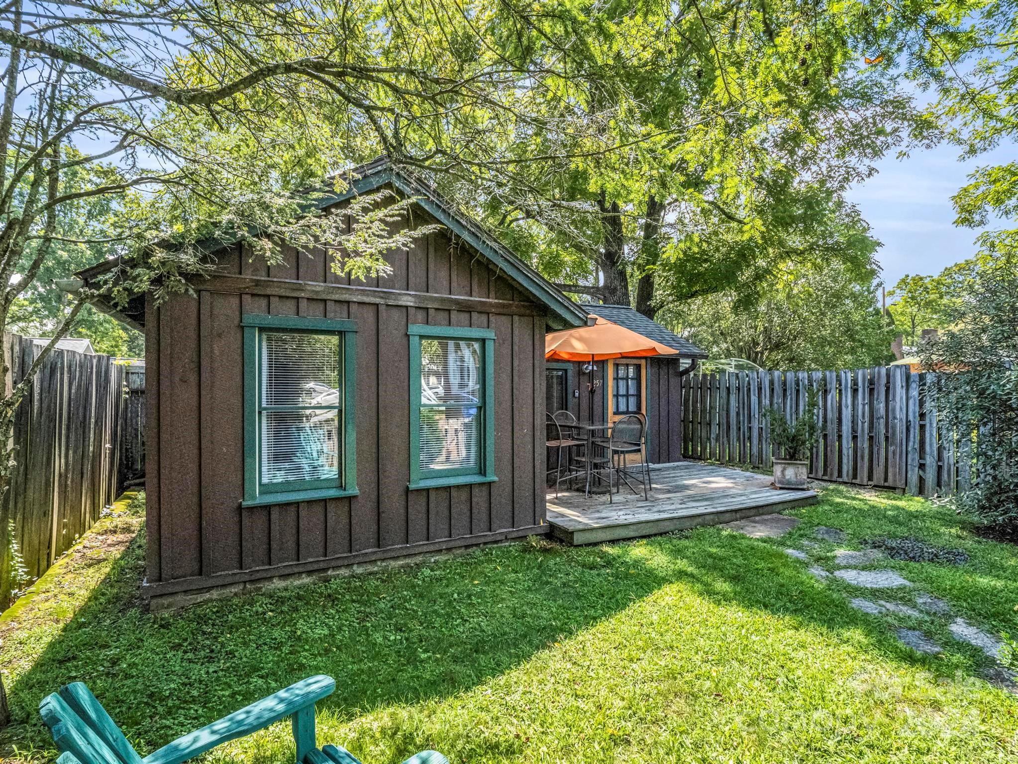 Brown-sided building with a shaded deck, patio furniture, orange umbrella, and stepping stones across the lawn.