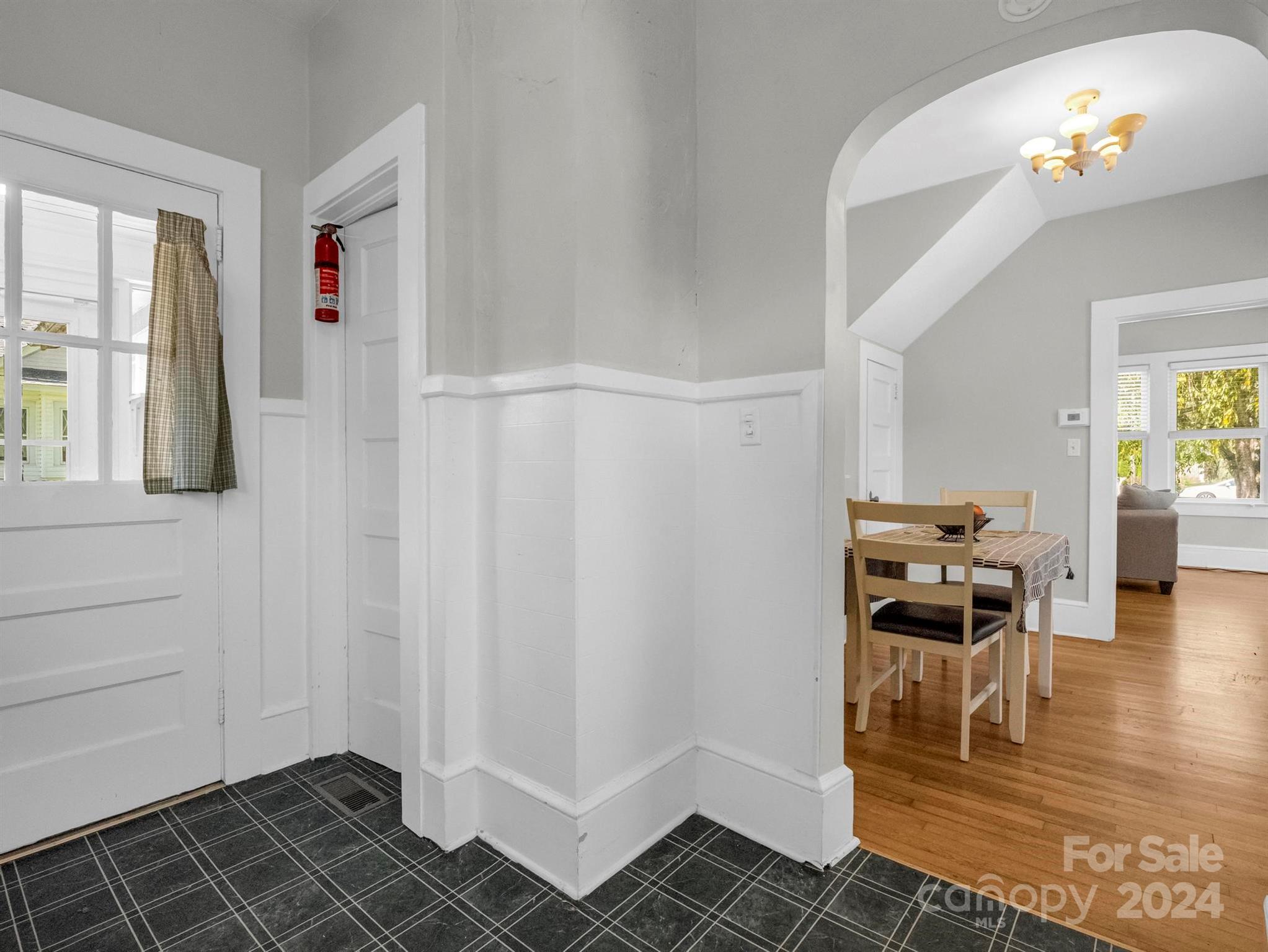 Entryway with dark tile flooring opens to a dining area with a wooden table and hardwood floors.