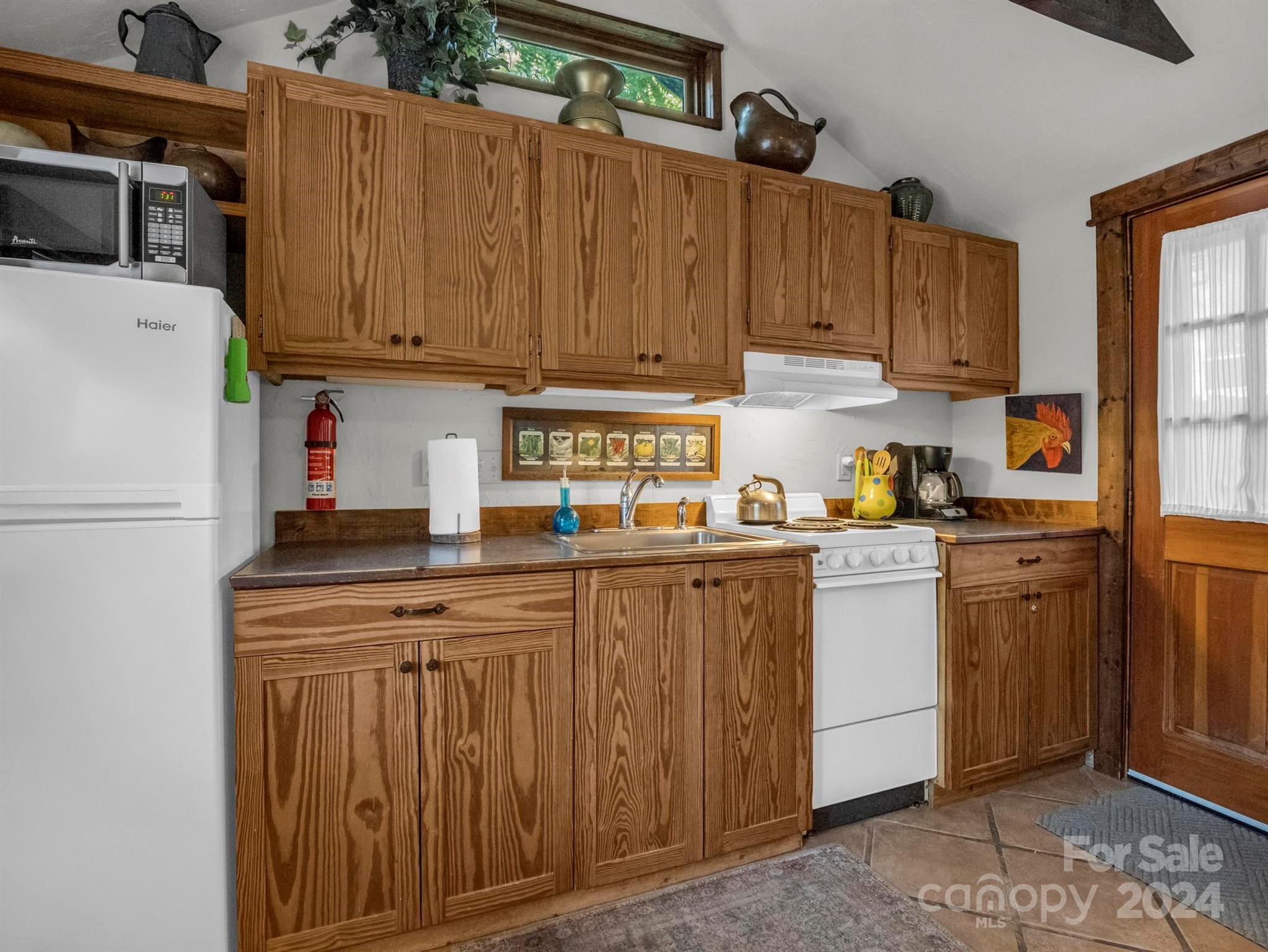 Kitchen with pine cabinets, white appliances, dark countertops, and a wood-framed door.