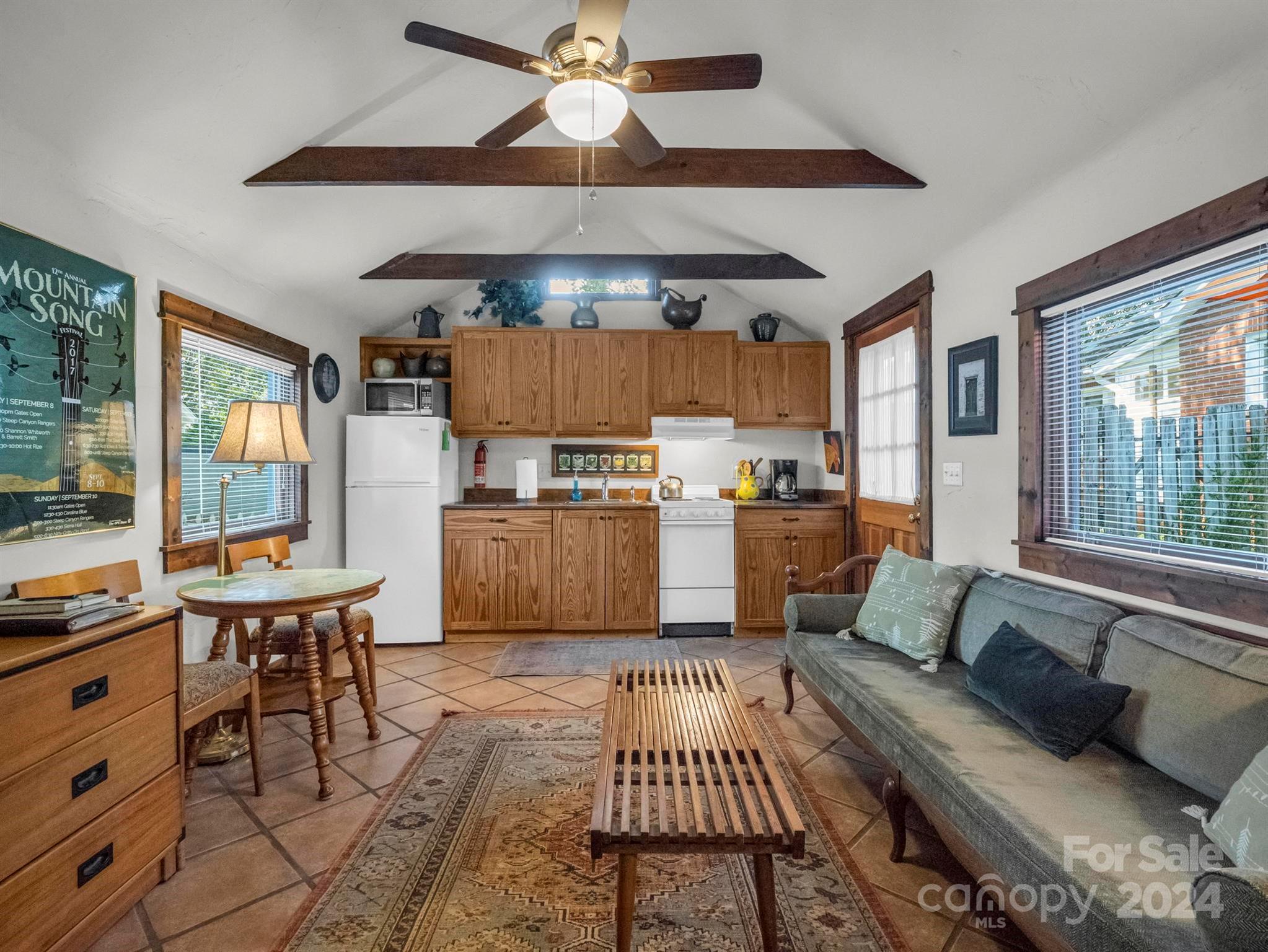Furnished kitchen and living area with wood cabinetry, tiled floors, and a vaulted beamed ceiling.