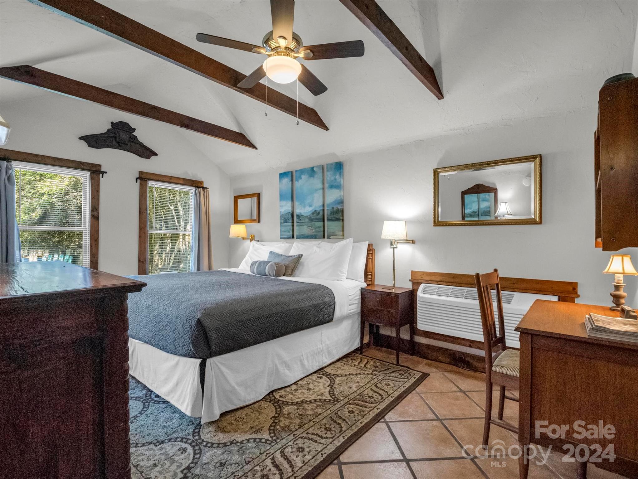 Furnished bedroom with a large bed beneath a vaulted ceiling with exposed wood beams.