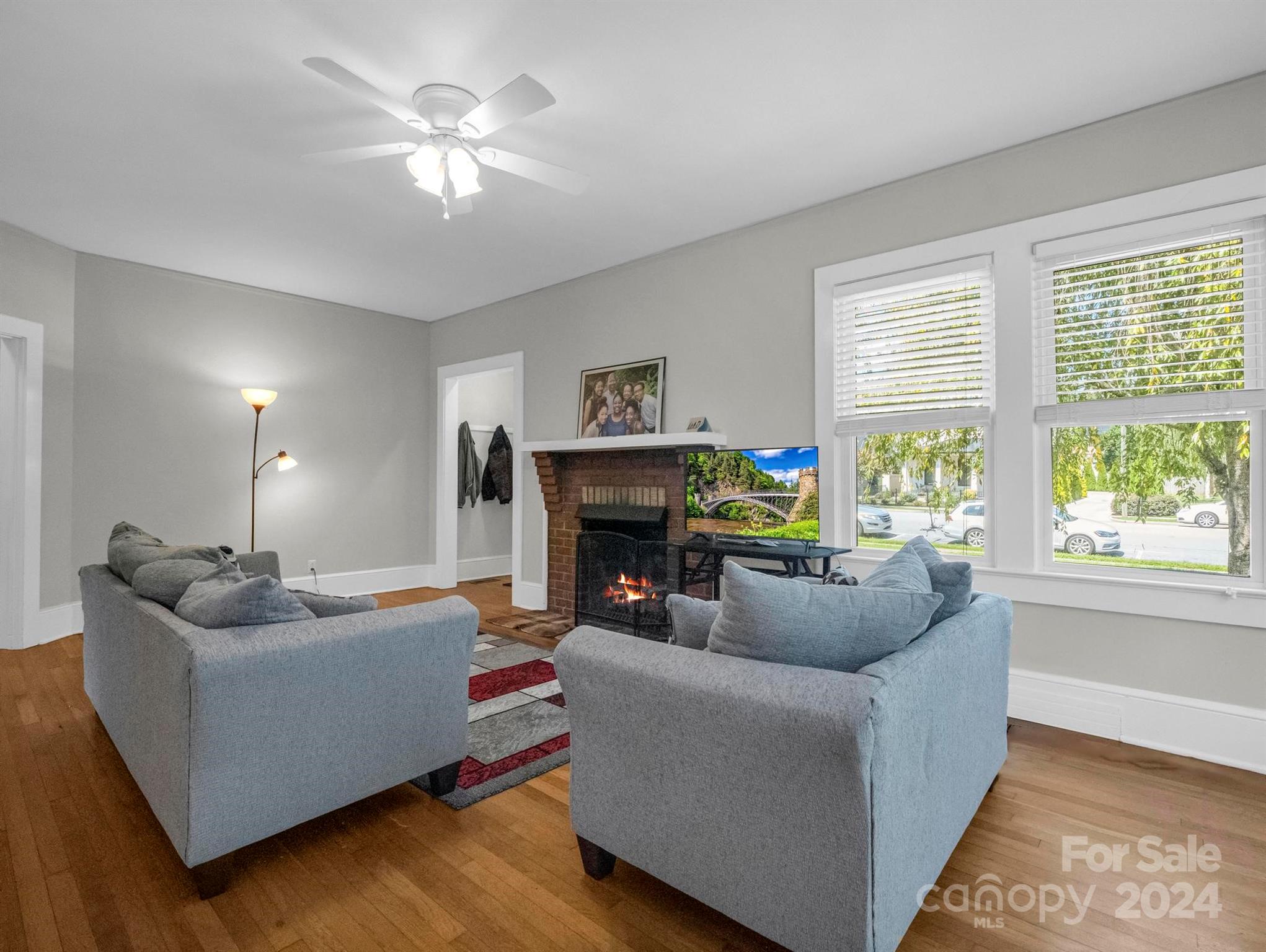 Living room with gray sofas, a brick fireplace, and large street-facing windows.