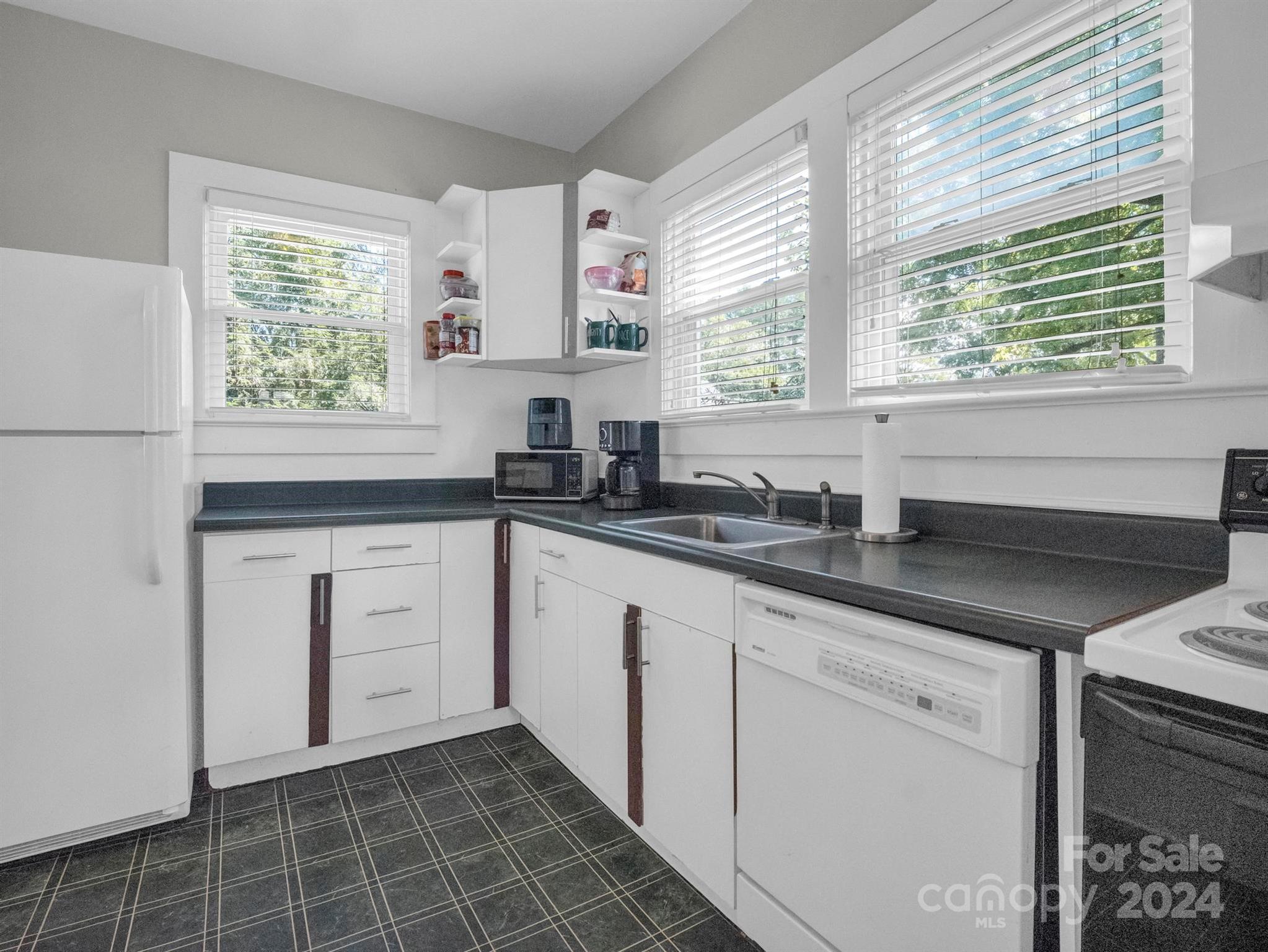 Kitchen with white cabinets, dark countertops, three windows, and a full set of appliances.