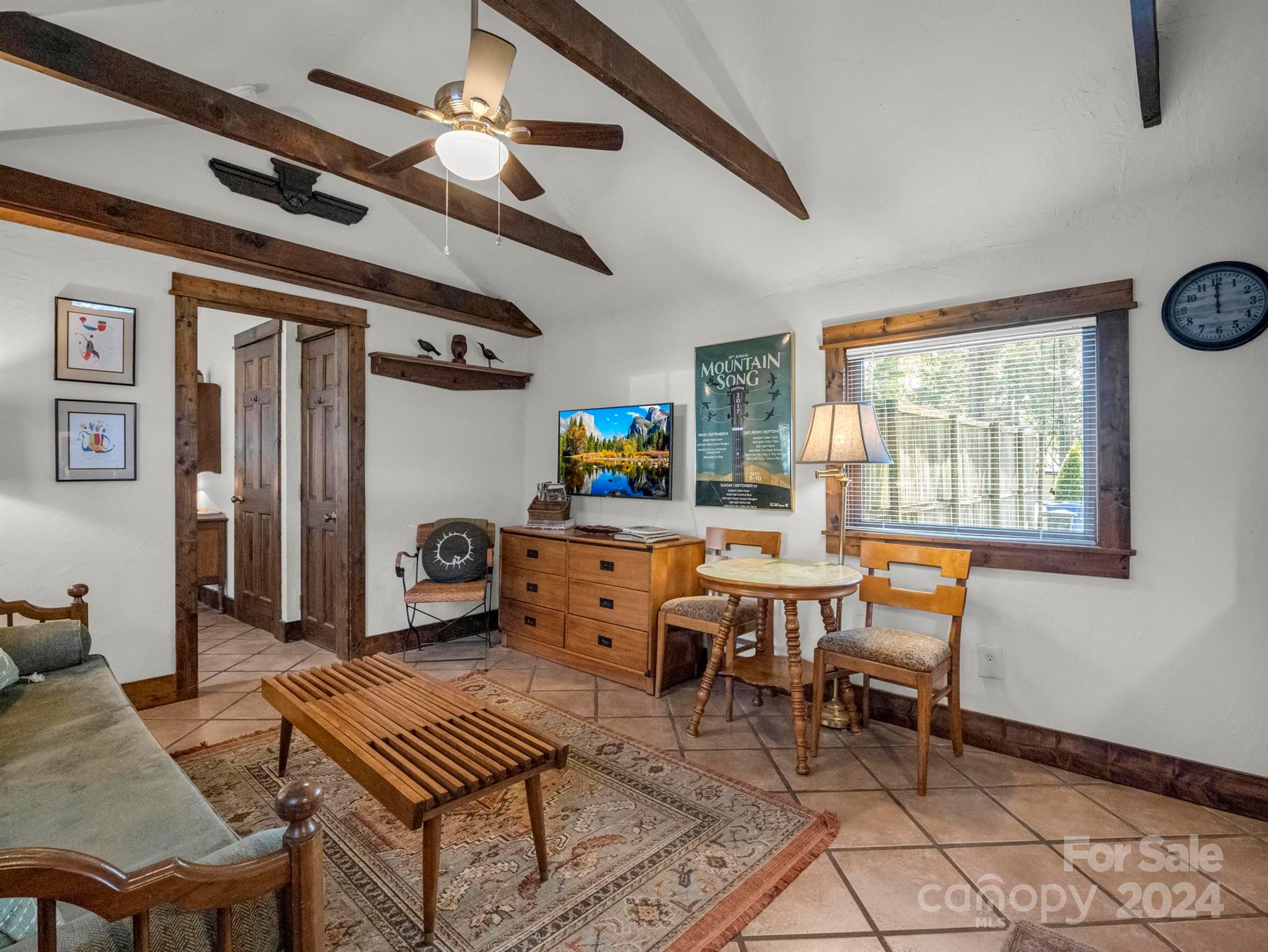 Furnished living room with exposed wood ceiling beams, tiled floors, and a small dining table.