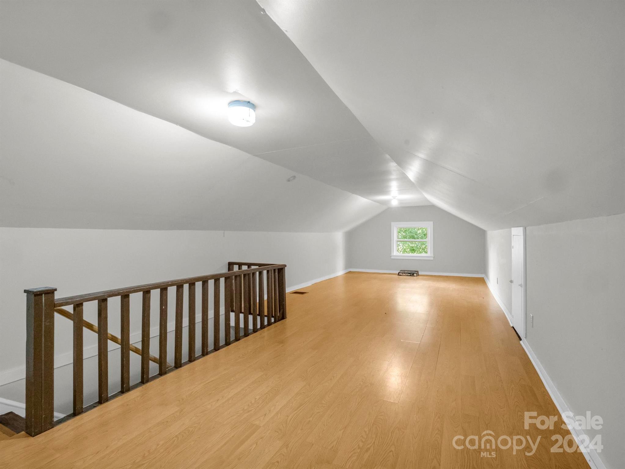 Finished attic loft with light wood floors, sloped ceiling, and railing around the stairwell.
