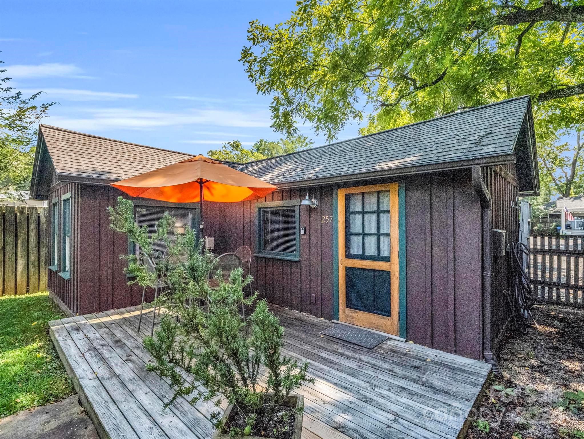 Dark wood-sided building with a weathered deck and bright orange patio umbrella.