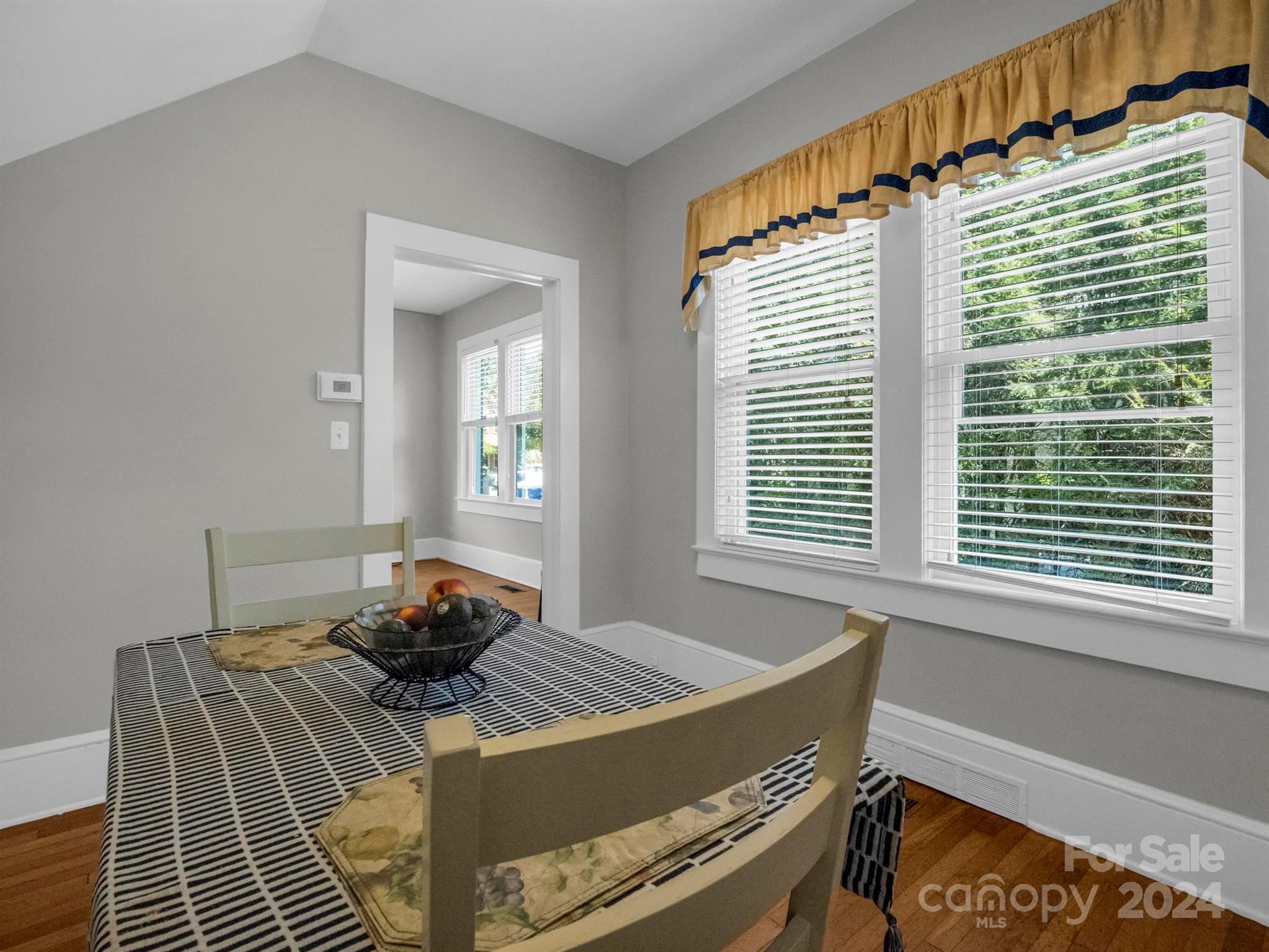 Dining room with a patterned table, light wood chairs, and large windows overlooking greenery.