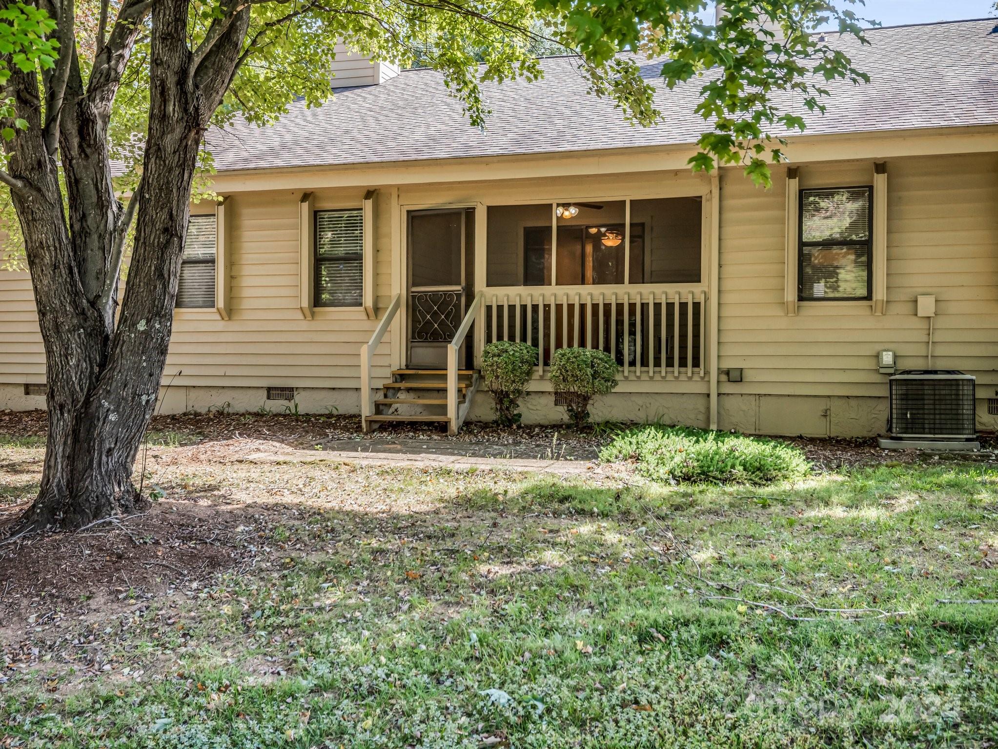 Beige-sided home with a covered porch and steps beneath mature shade trees.