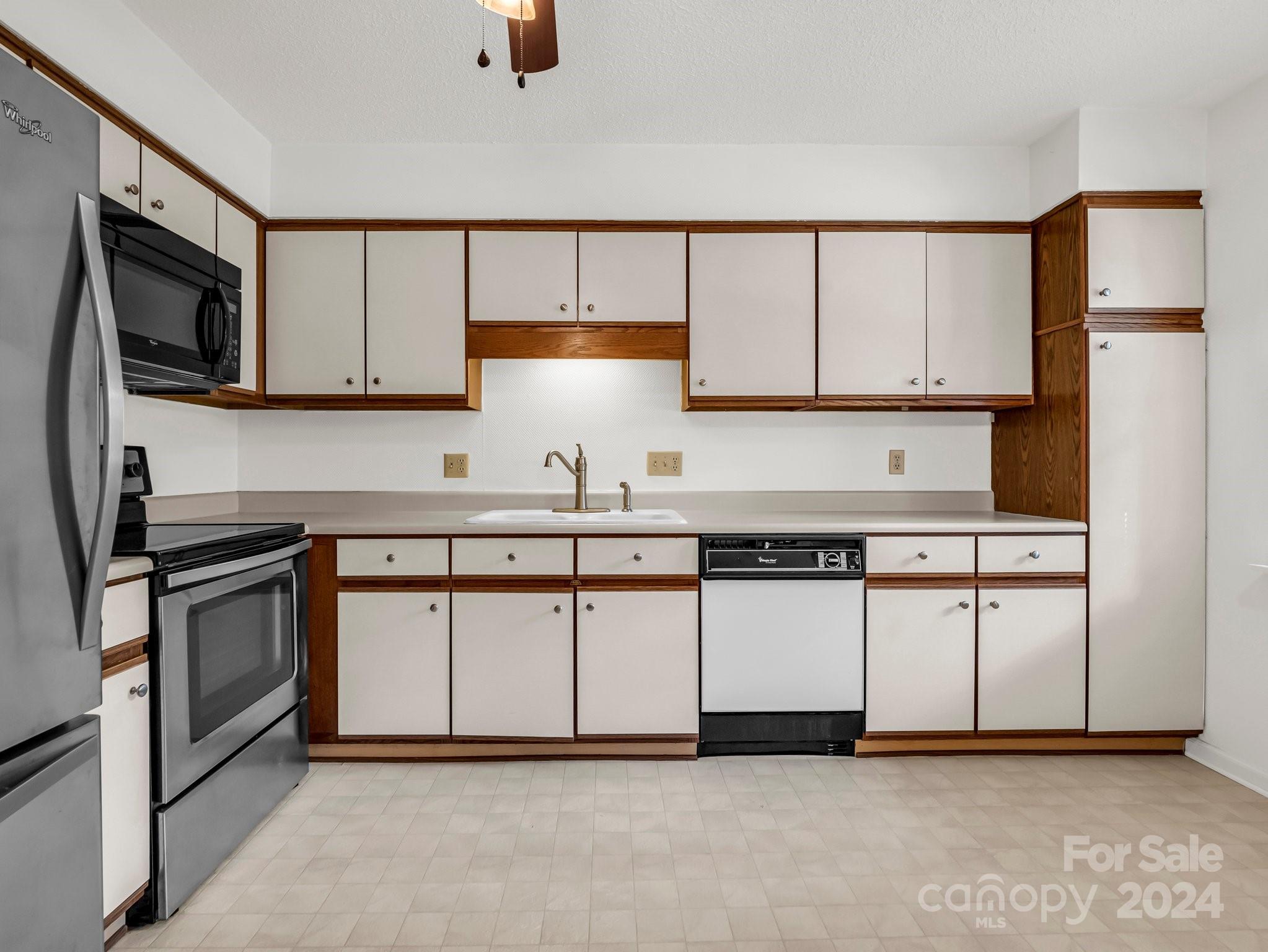 Kitchen with white and dark wood cabinets, stainless-steel appliances, and a tiled floor.