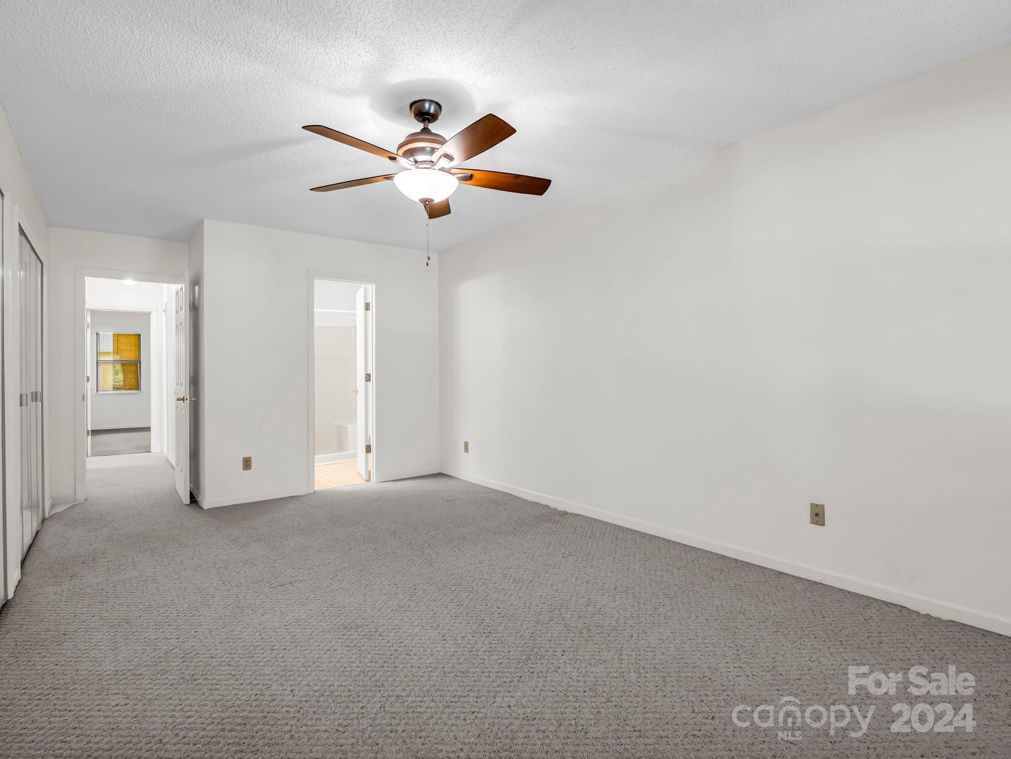 Empty bedroom with gray carpet, a wooden-blade ceiling fan, and doorways to adjoining rooms.