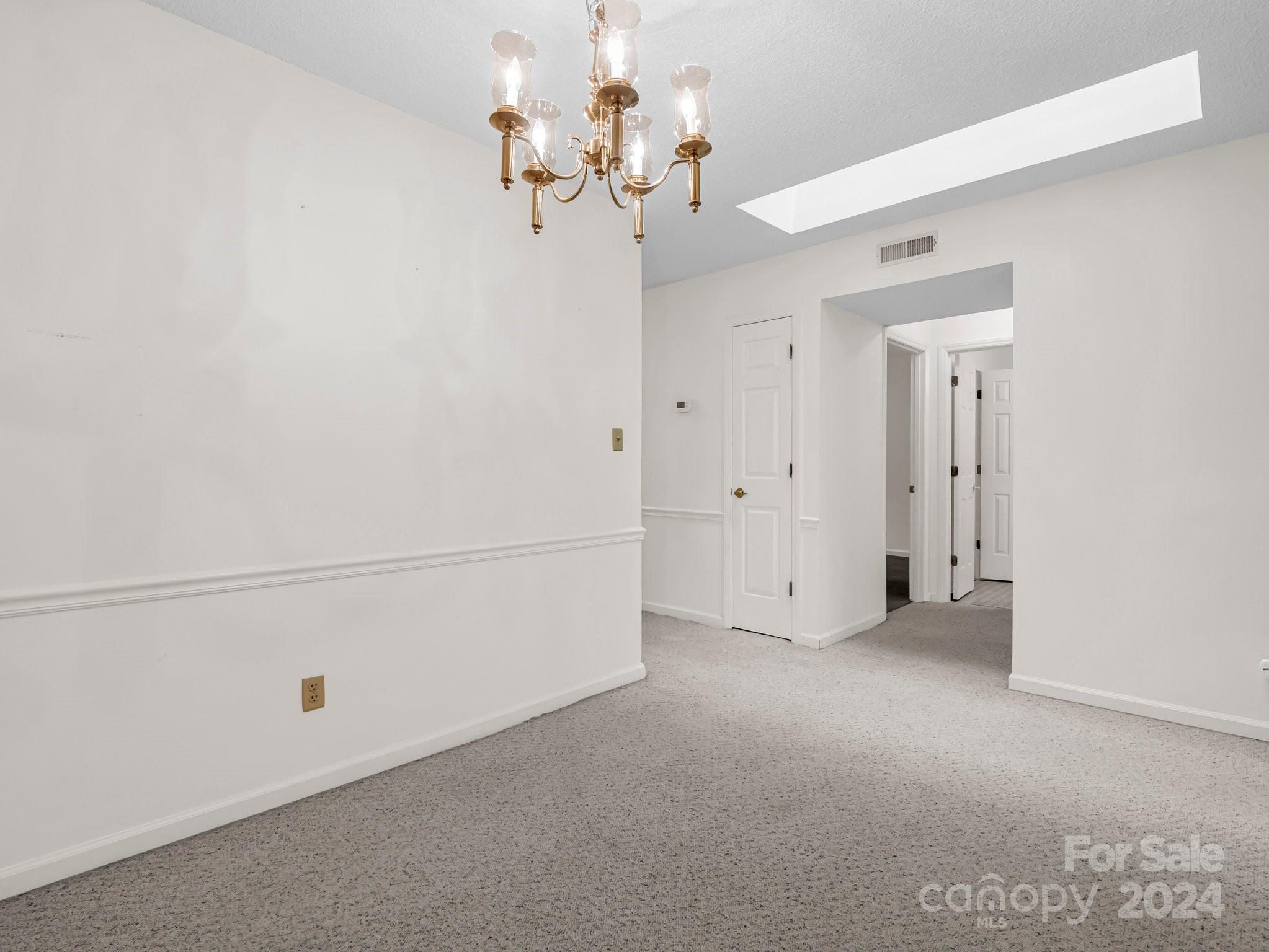 Empty carpeted room with a brass chandelier, skylight, and doorway to adjoining rooms.