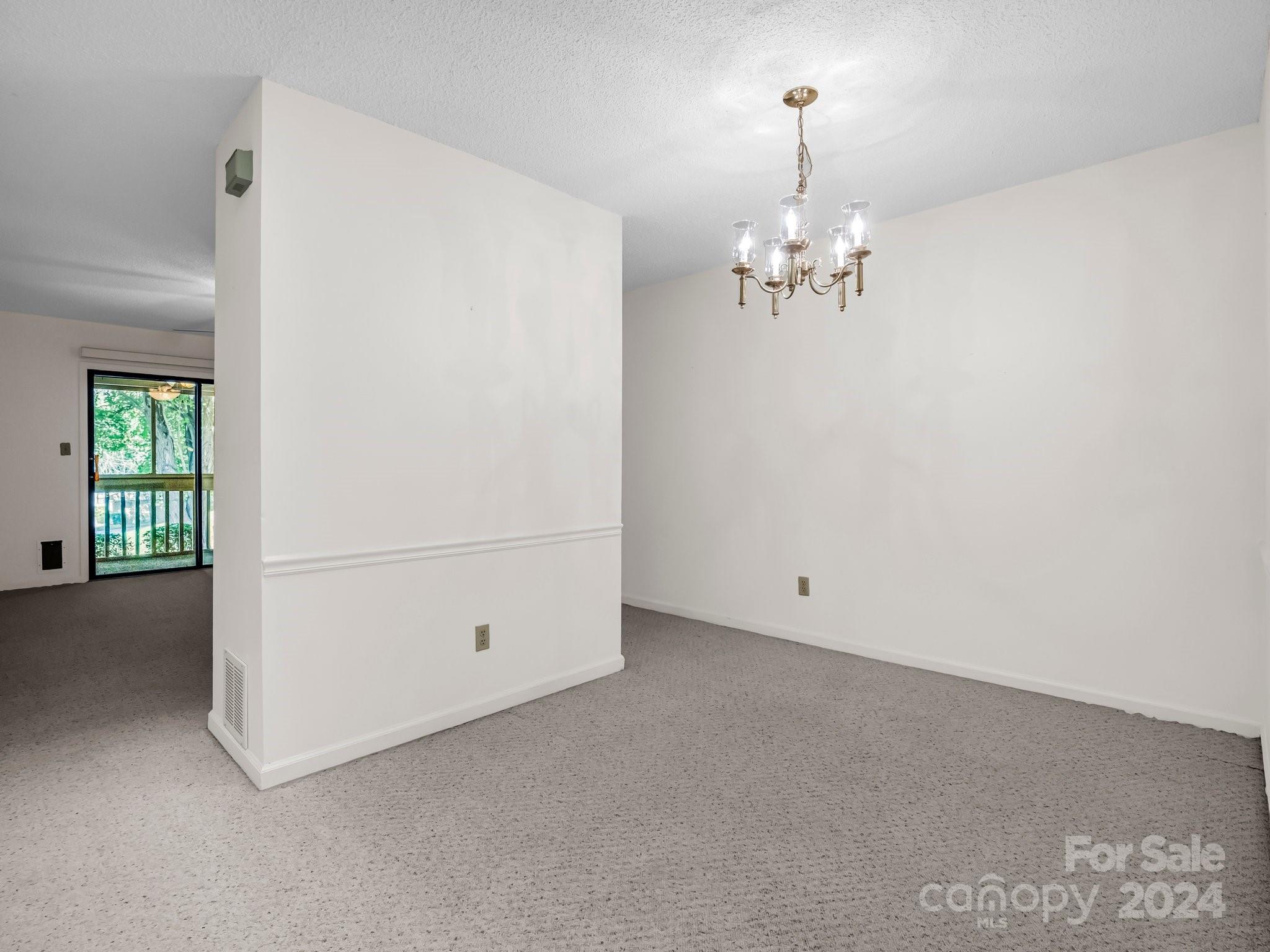 Empty dining room with a brass chandelier and sliding glass door overlooking trees.