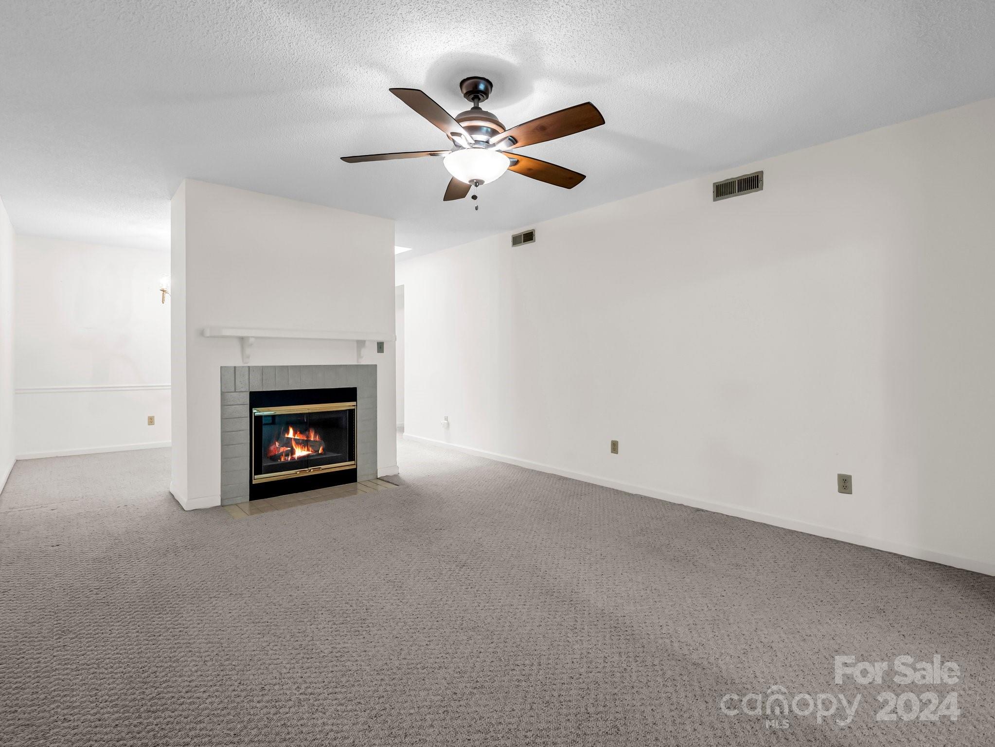 Empty living room with a lit gray-tile fireplace and a wooden-blade ceiling fan.