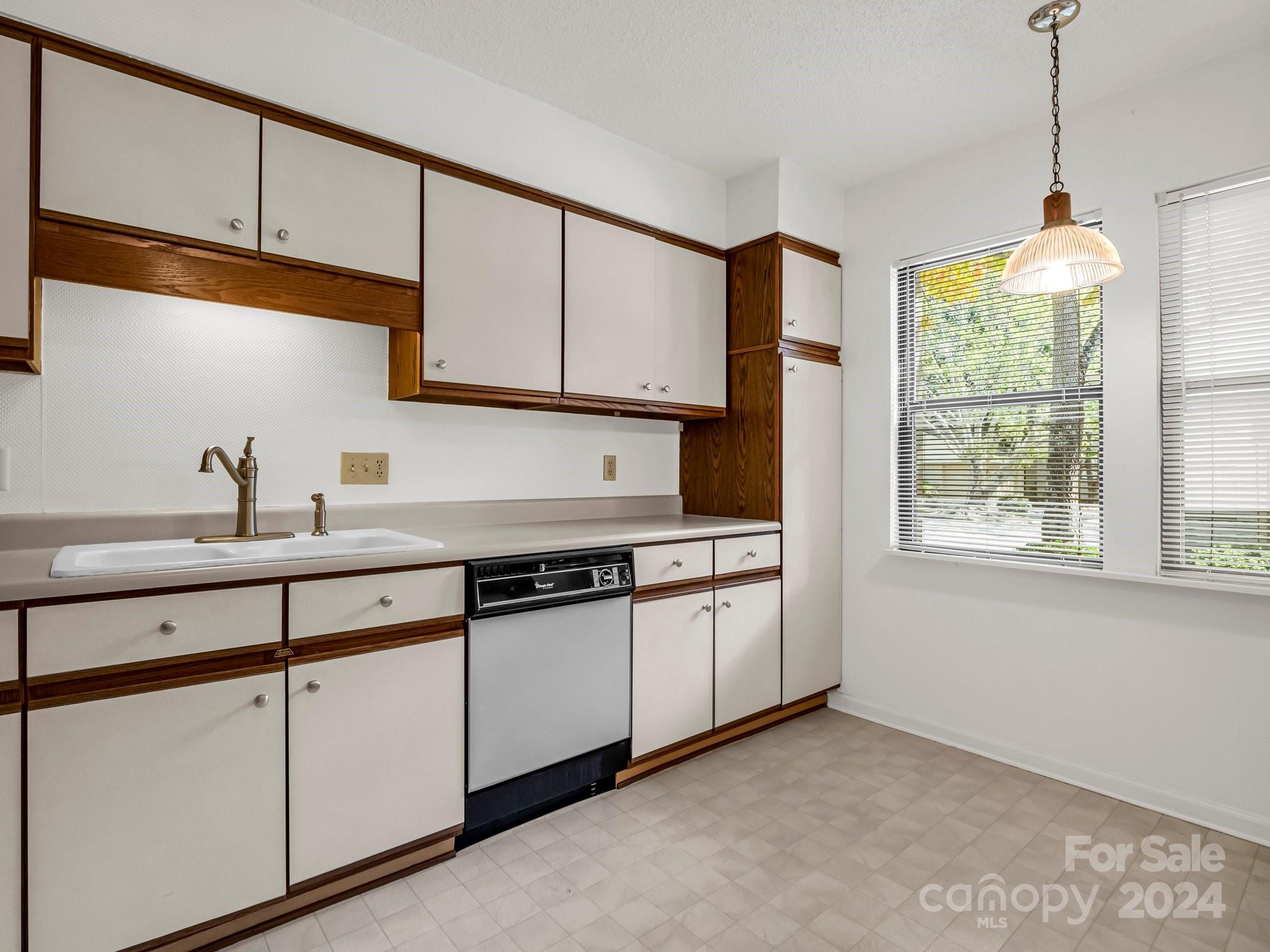 Kitchen with white and dark wood cabinets, a sink, dishwasher, and windows with blinds.