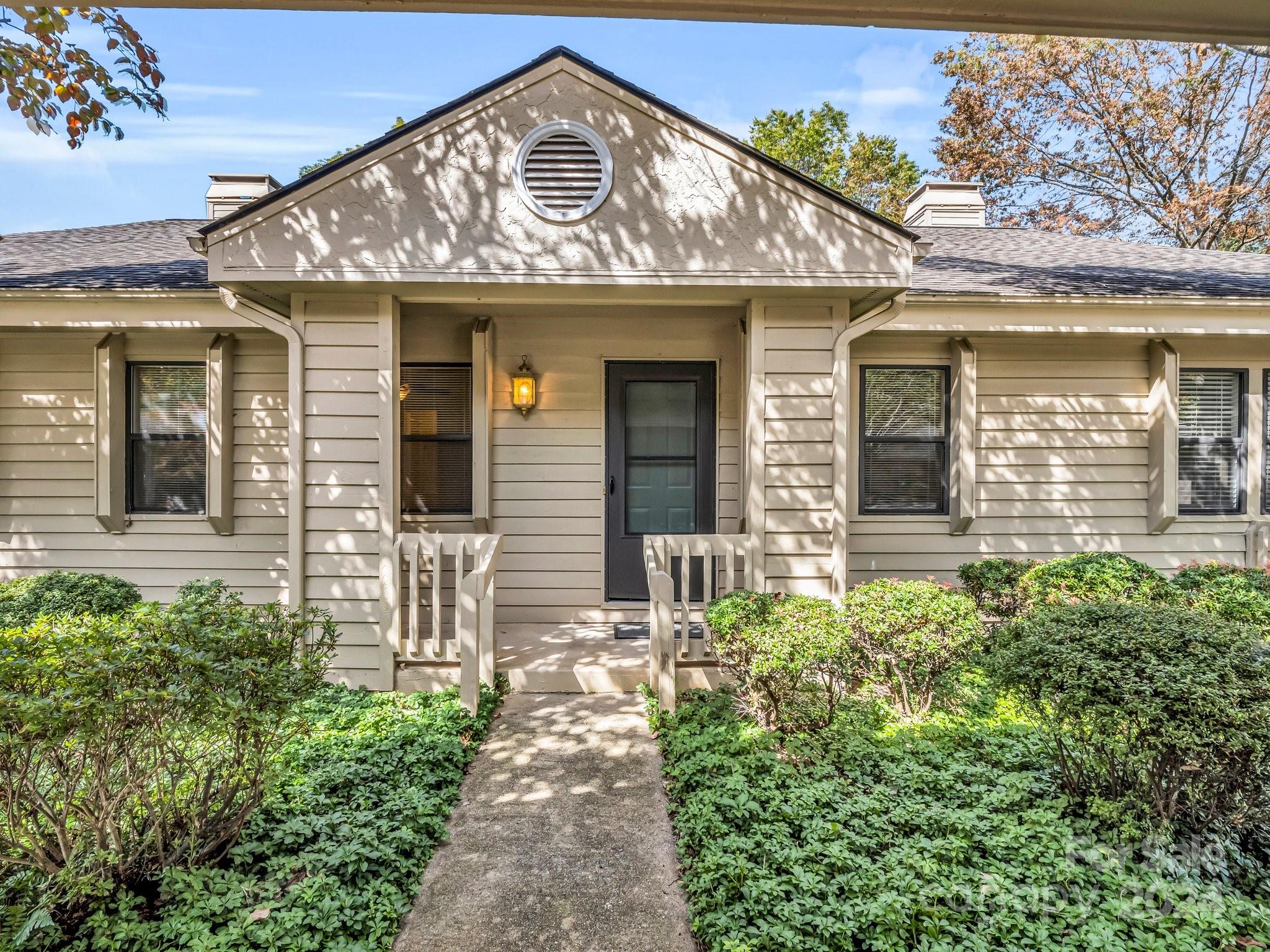 Beige-sided home with a peaked entry, dark front door, and shrubs bordering the walkway.