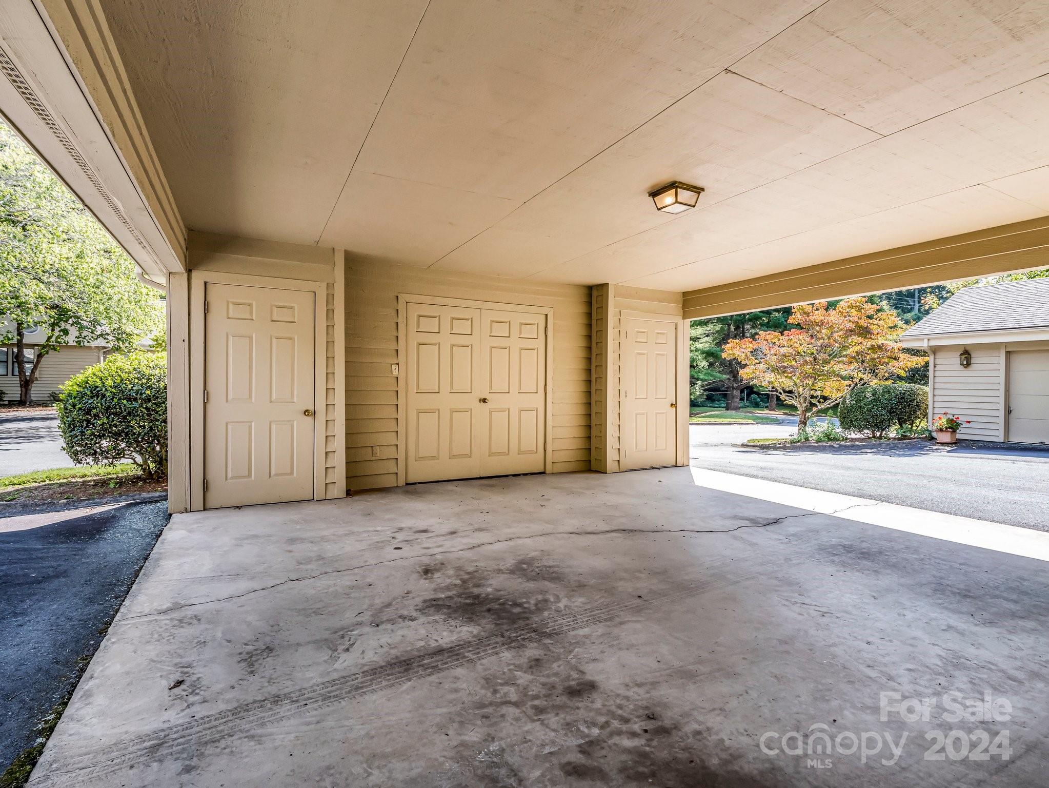 Covered carport with three paneled doors and a broad concrete floor.