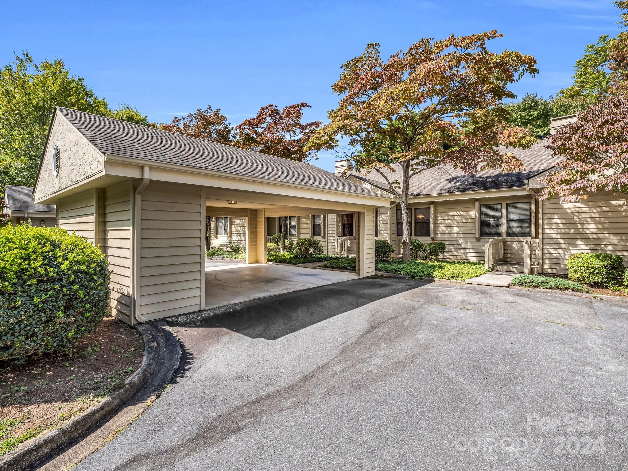 Beige-sided home with a covered carport, paved driveway, and autumn trees.