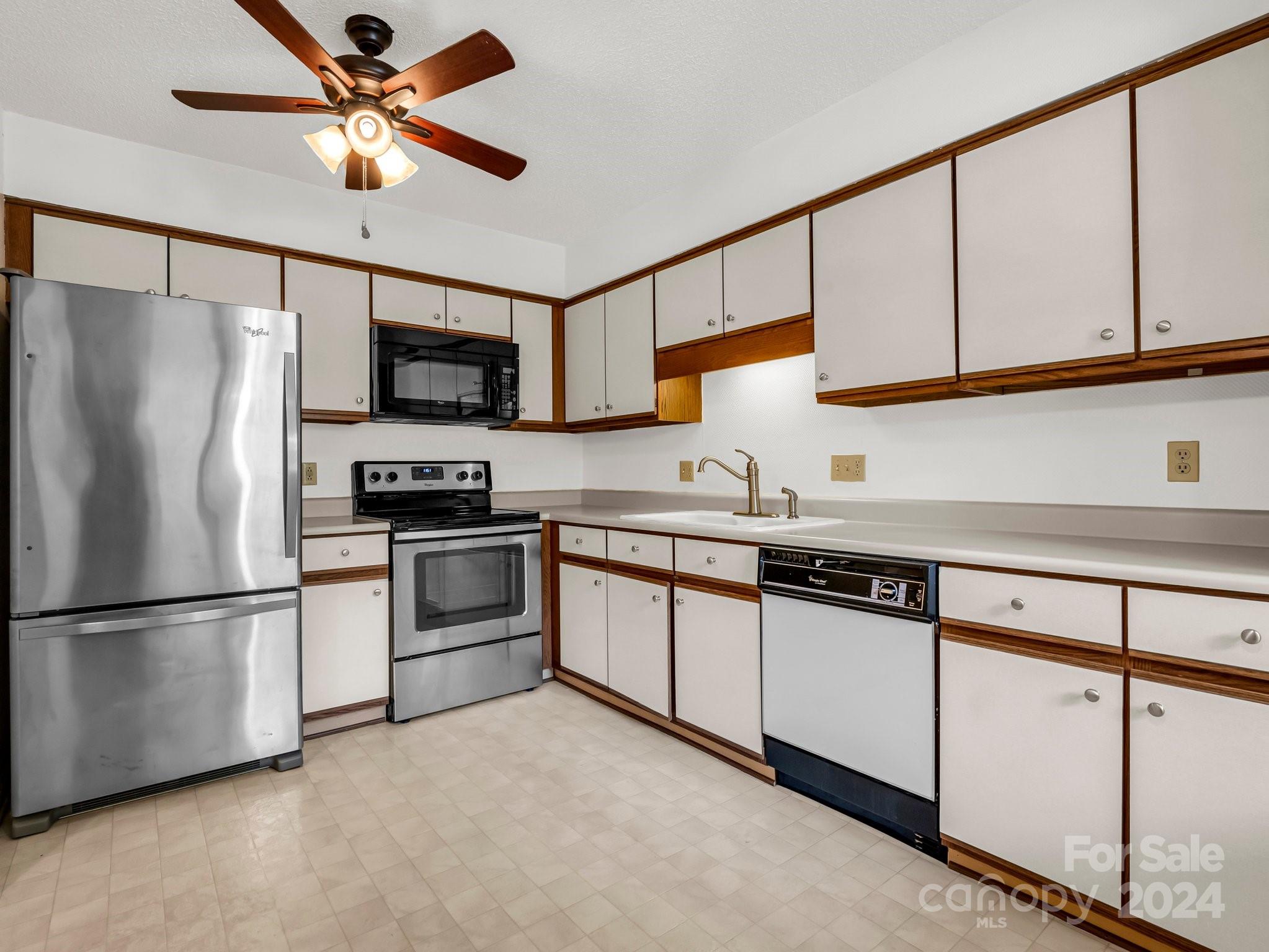 Kitchen with white and wood-trimmed cabinets, stainless steel appliances, and a ceiling fan.