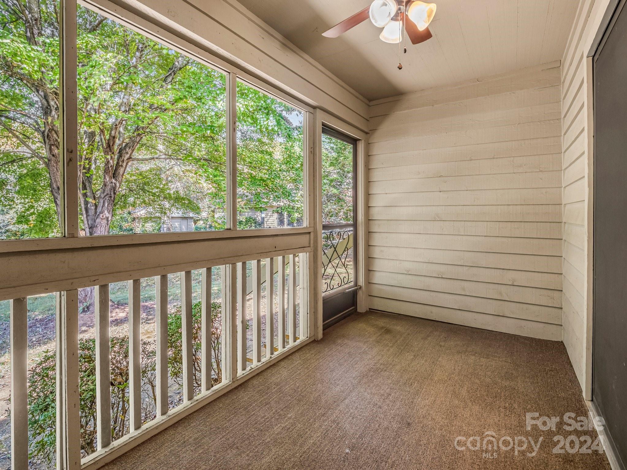 Covered porch with large screened windows, white railing and leafy trees outside.