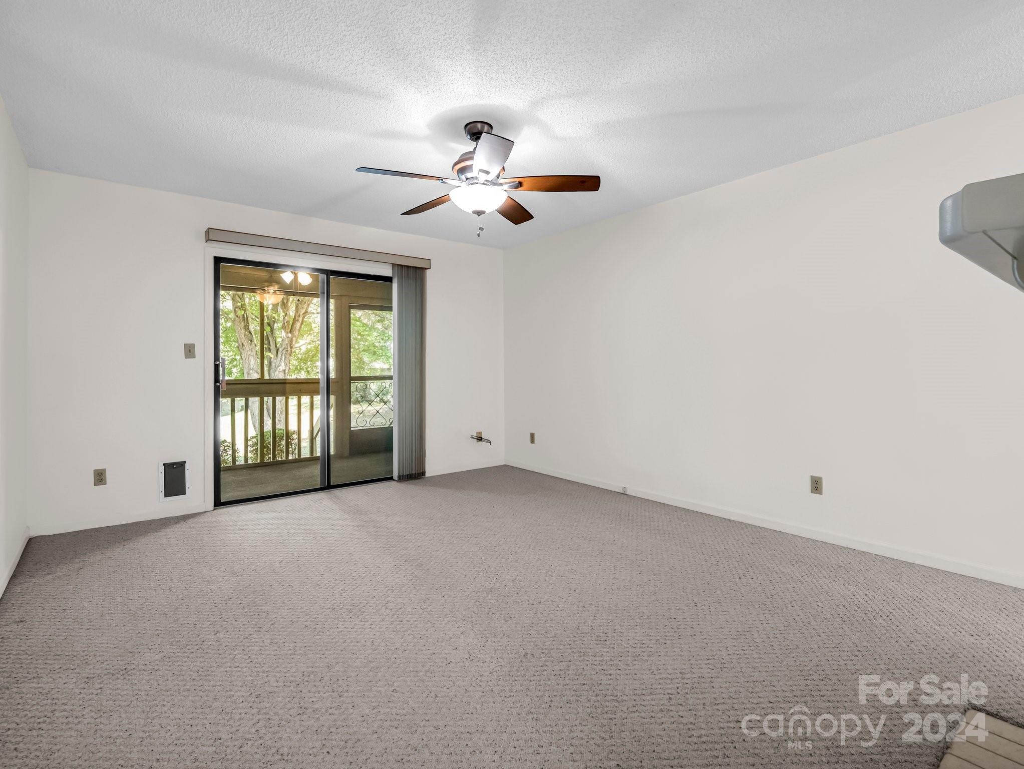 Vacant carpeted room with a ceiling fan and sliding doors to a balcony.