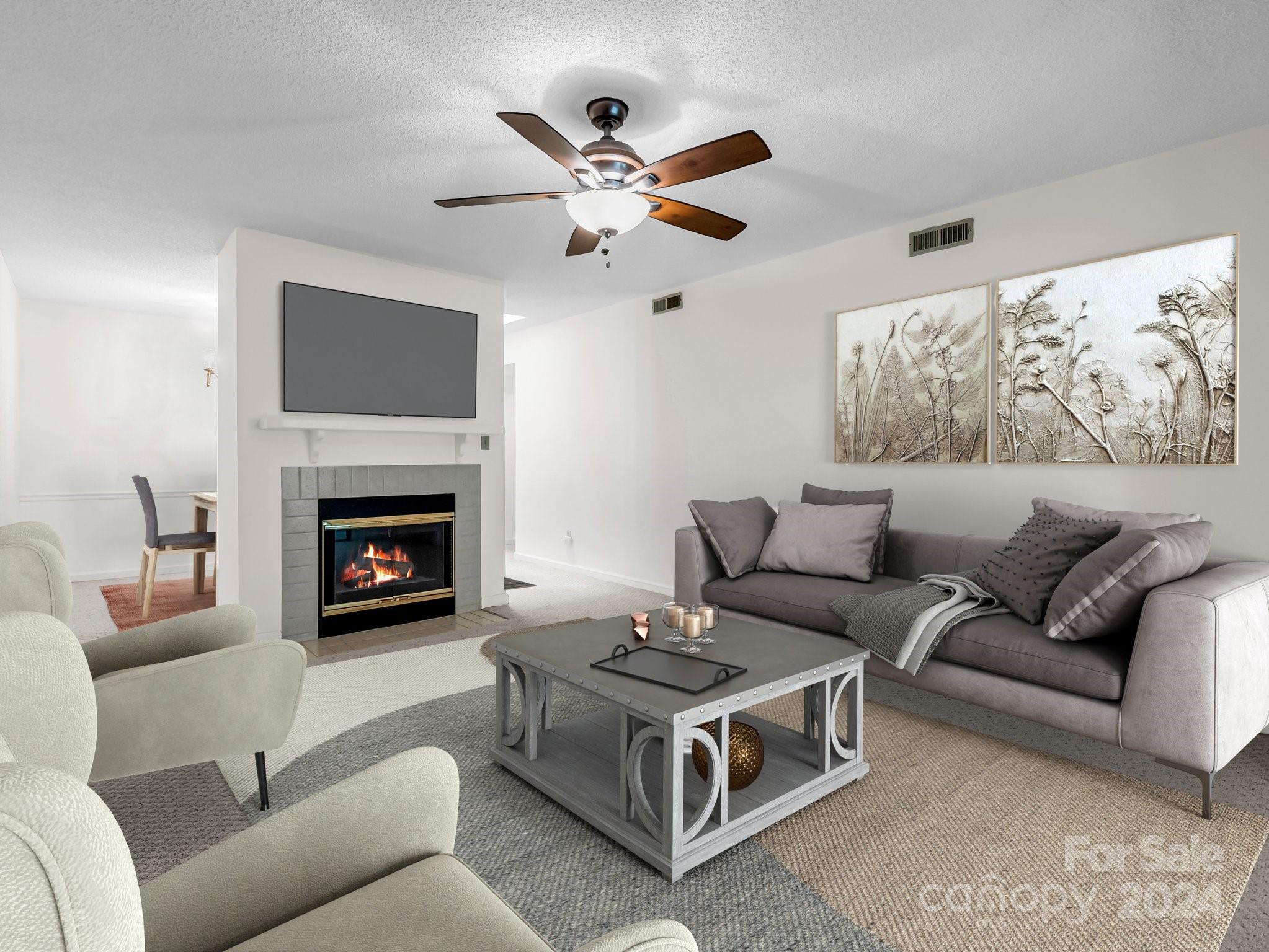 Staged living room with gray seating around a coffee table and a lit fireplace beneath a mounted television.