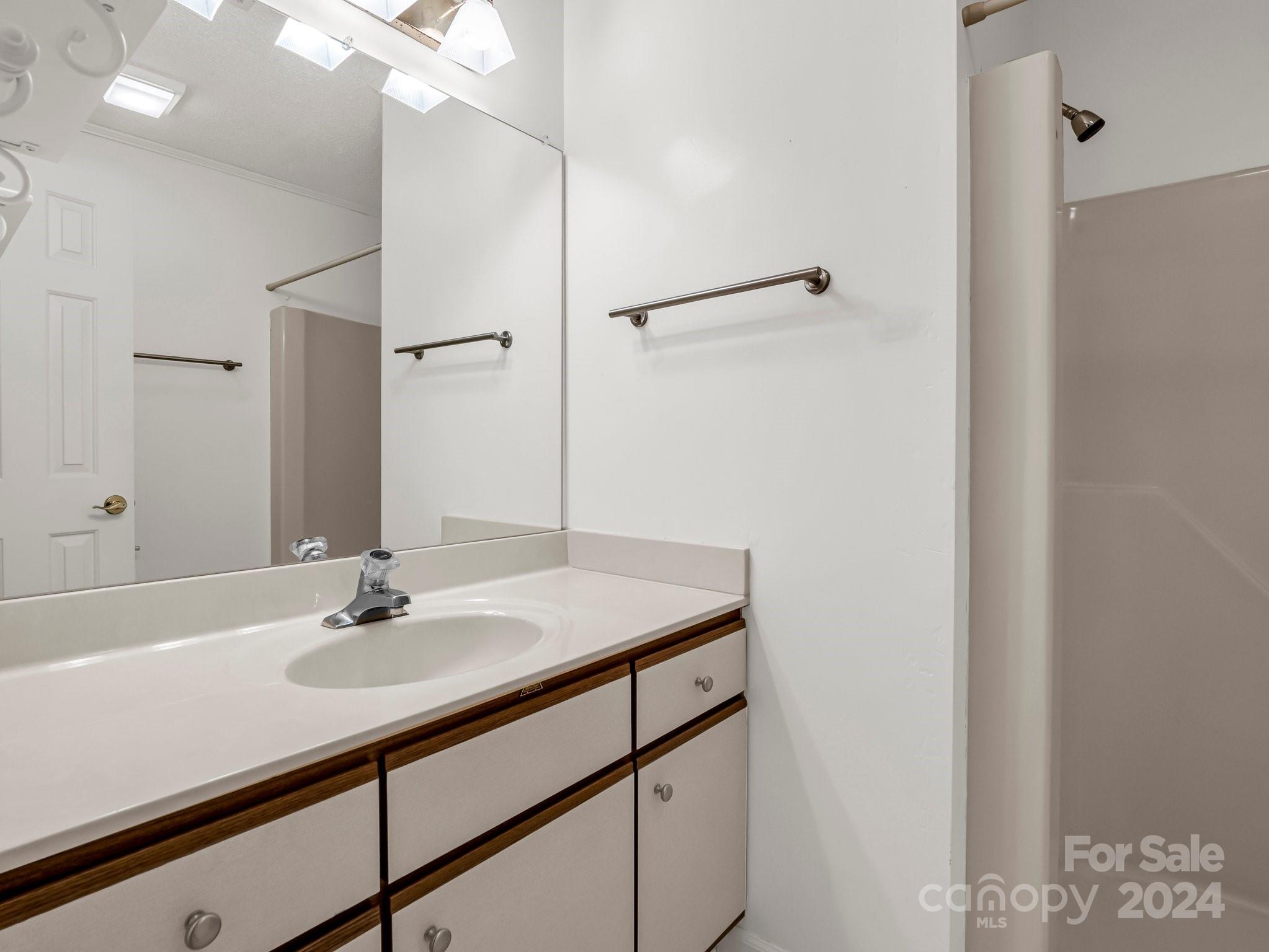 Bathroom vanity with an oval sink, mirrored wall, and wood-trimmed cabinets.