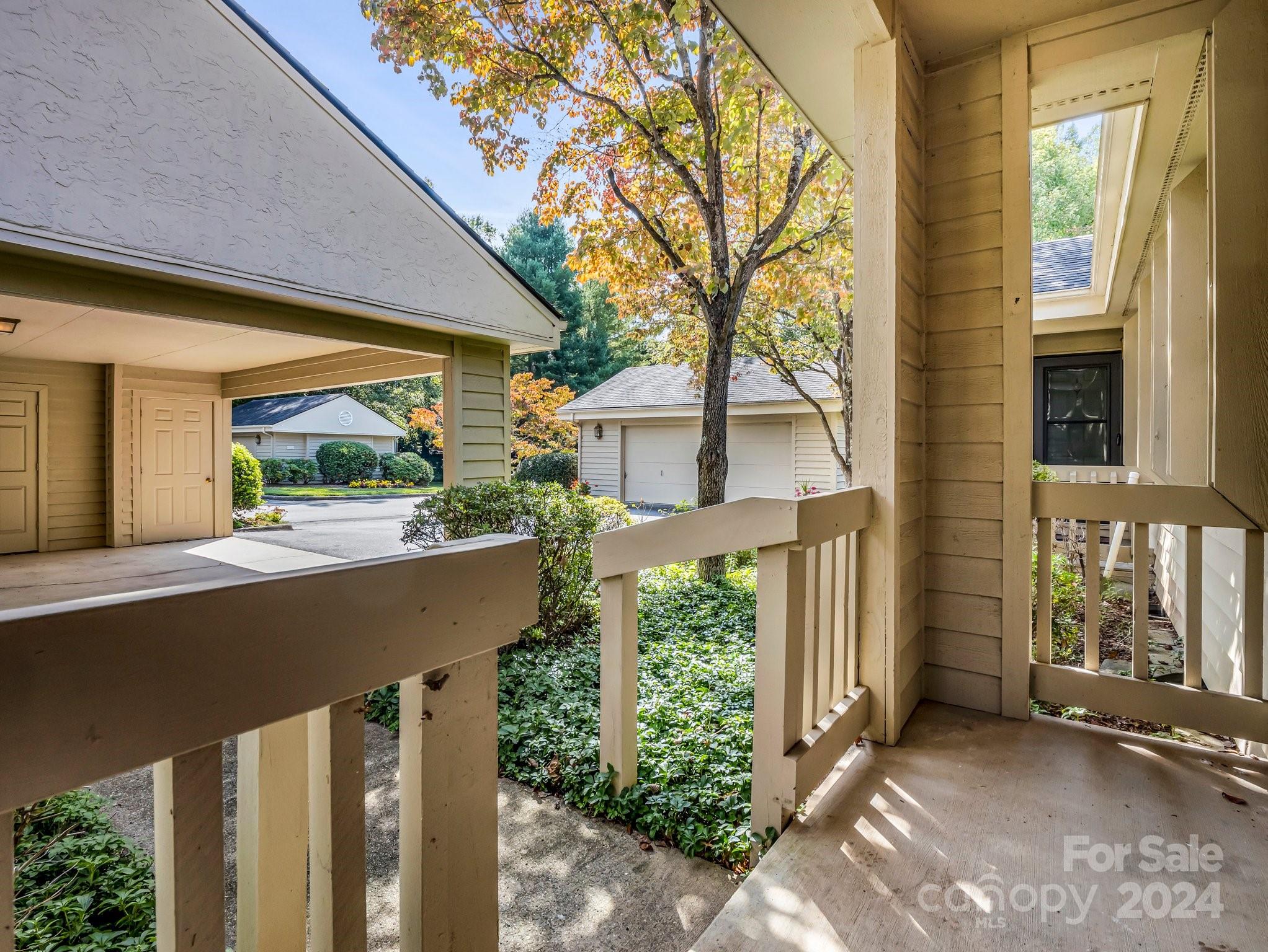 Covered porch with beige railings overlooks landscaped grounds and neighboring garages in autumn.