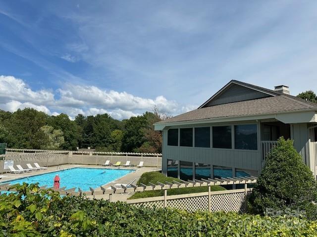Outdoor pool beside a gray-sided building, with lounge chairs and leafy landscaping.