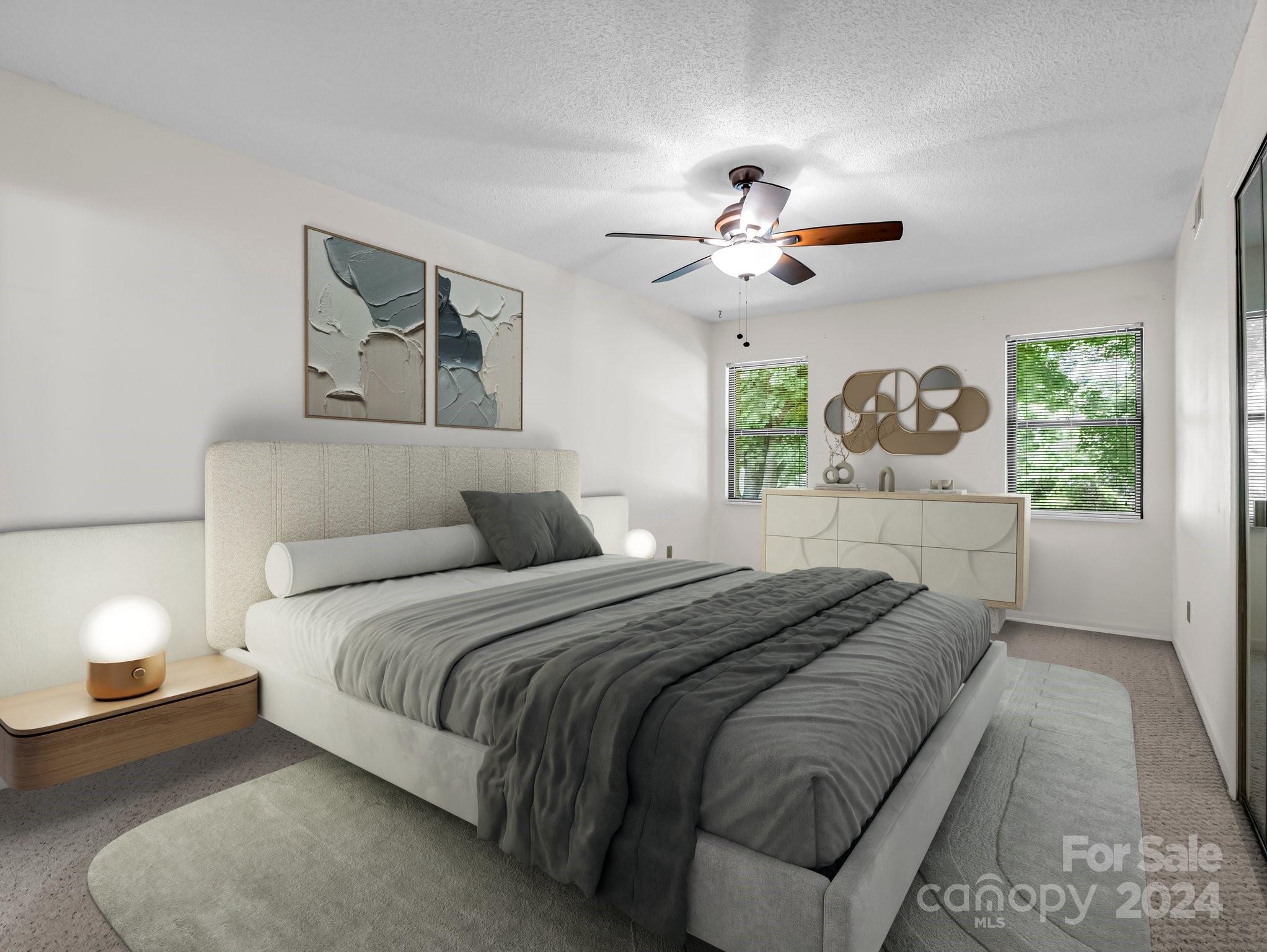 Furnished bedroom with a large gray bed, abstract wall art, and windows overlooking greenery.