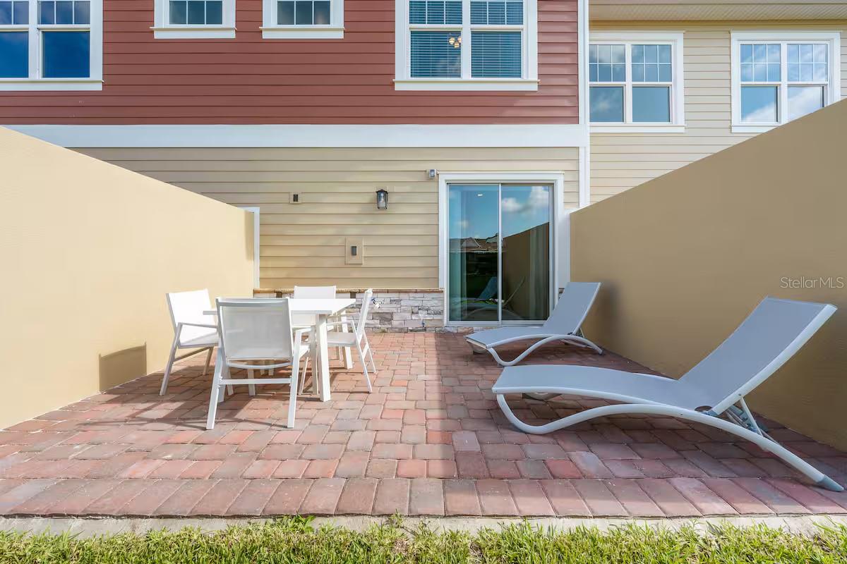 Backyard patio with pavers, a white dining set, two chaise lounges, and a sliding glass door.