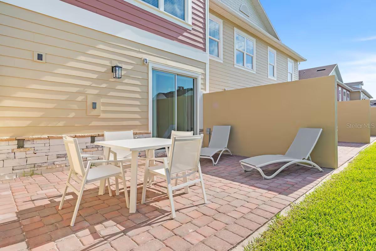 Paved home patio with outdoor dining set, two chaise lounges, and a tan privacy partition.